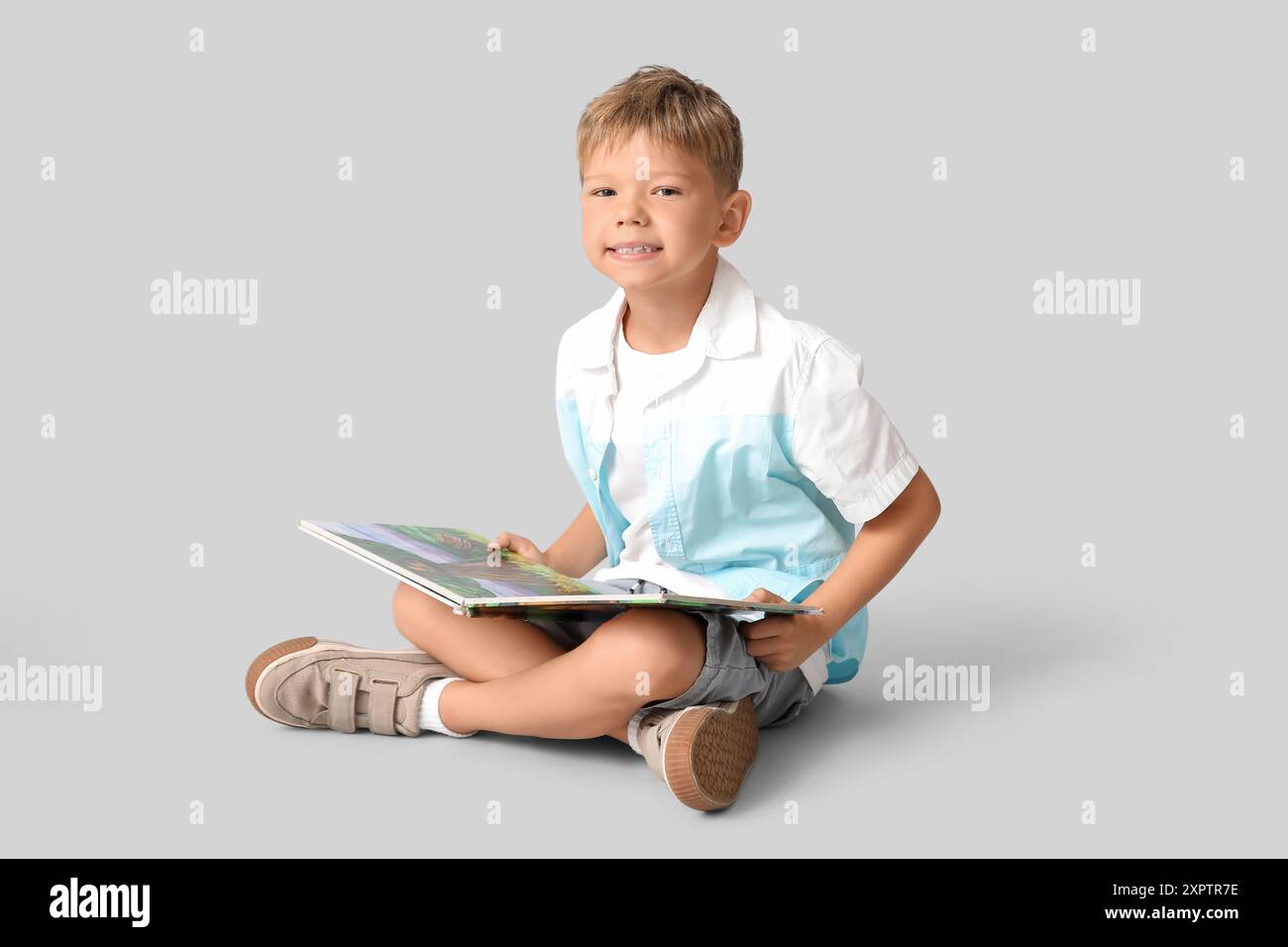 Portrait of cute little boy sitting on floor and reading book on grey ...