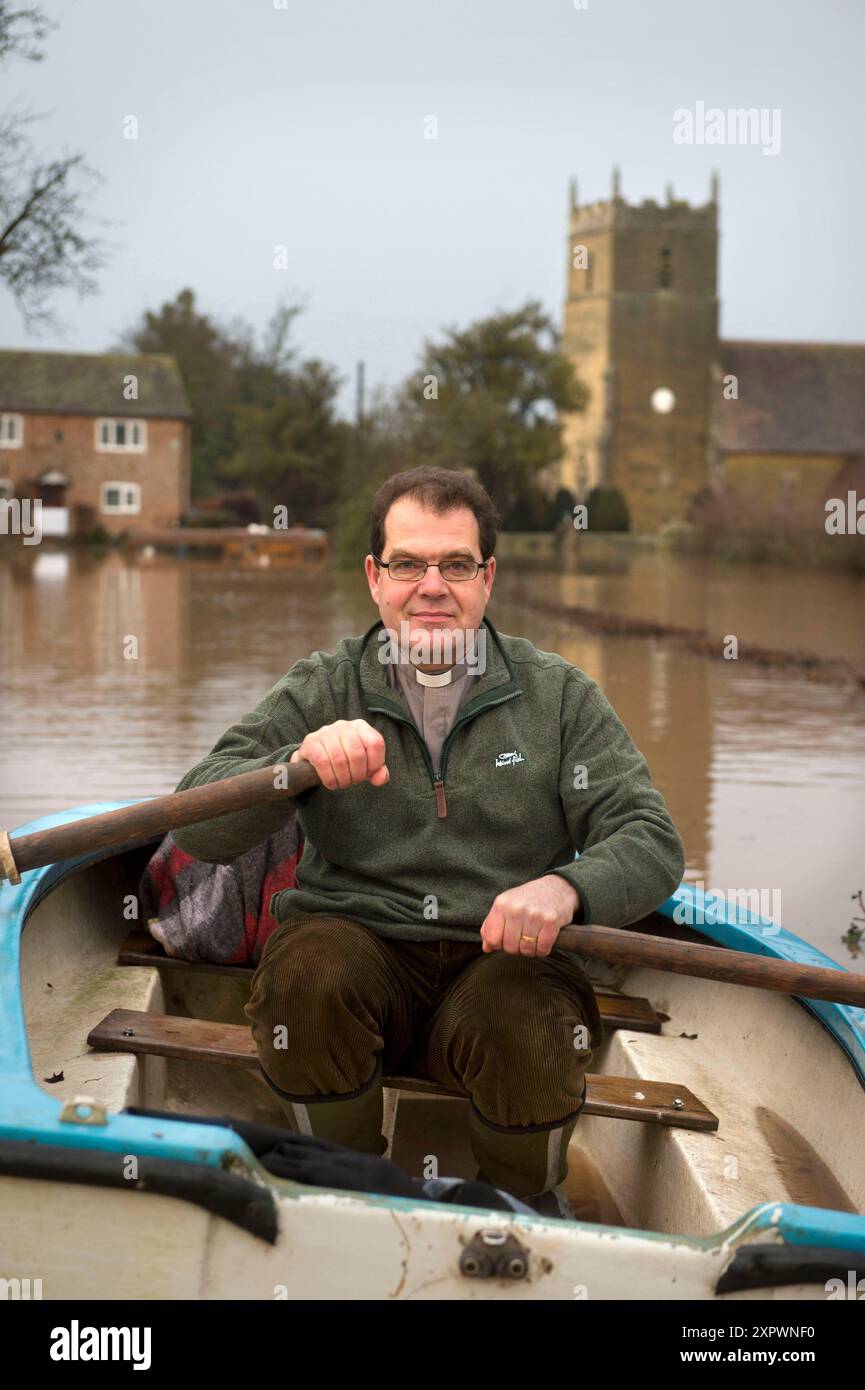 The Revd John Longuet-Higgins negotiates flood water from the River Severn to check on the marooned church of St Michael's and All Angel's at Tirley, Stock Photo