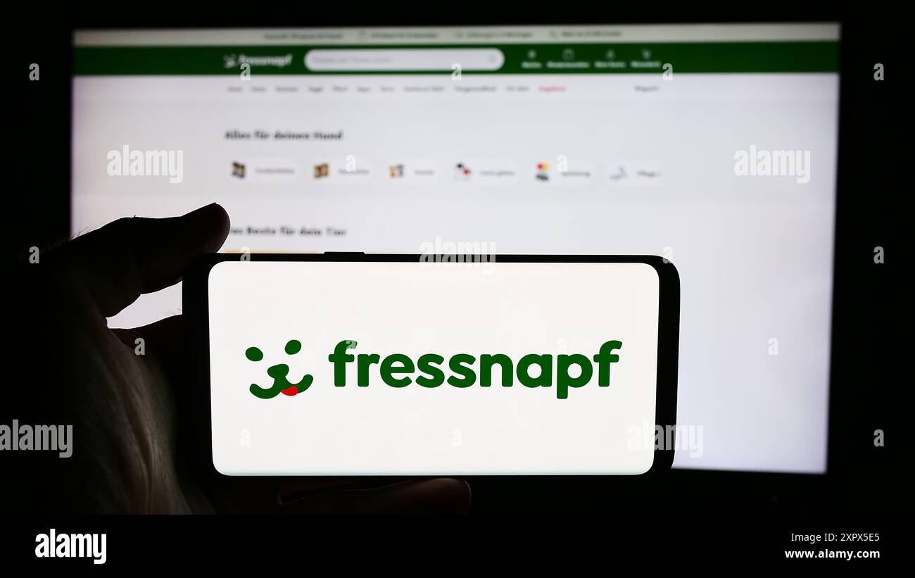 Person holding cellphone with logo of German retail company Fressnapf Holding SE in front of business webpage. Focus on phone display. Stock Photo