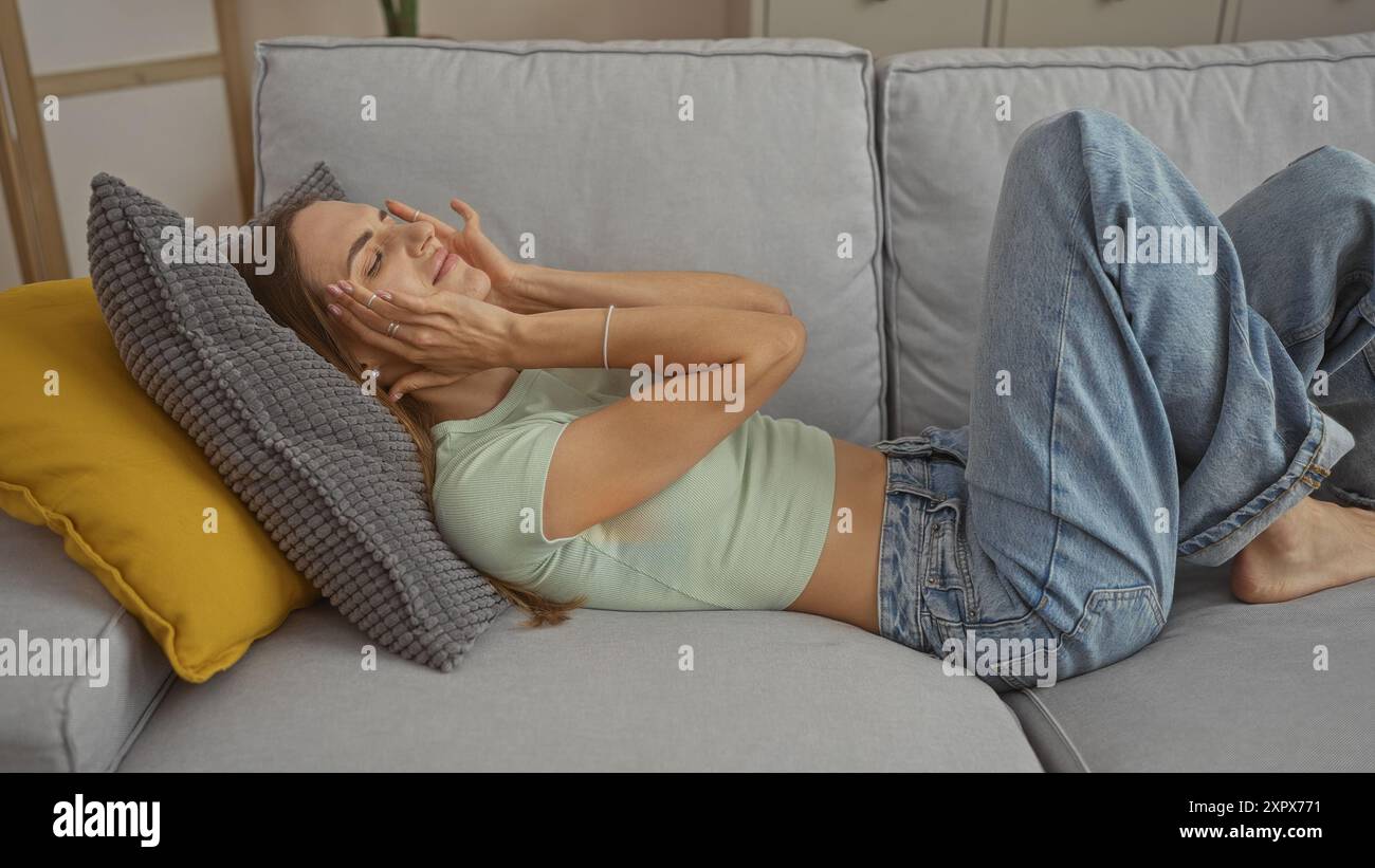 A young beautiful blonde woman relaxes on a comfortable couch indoors ...