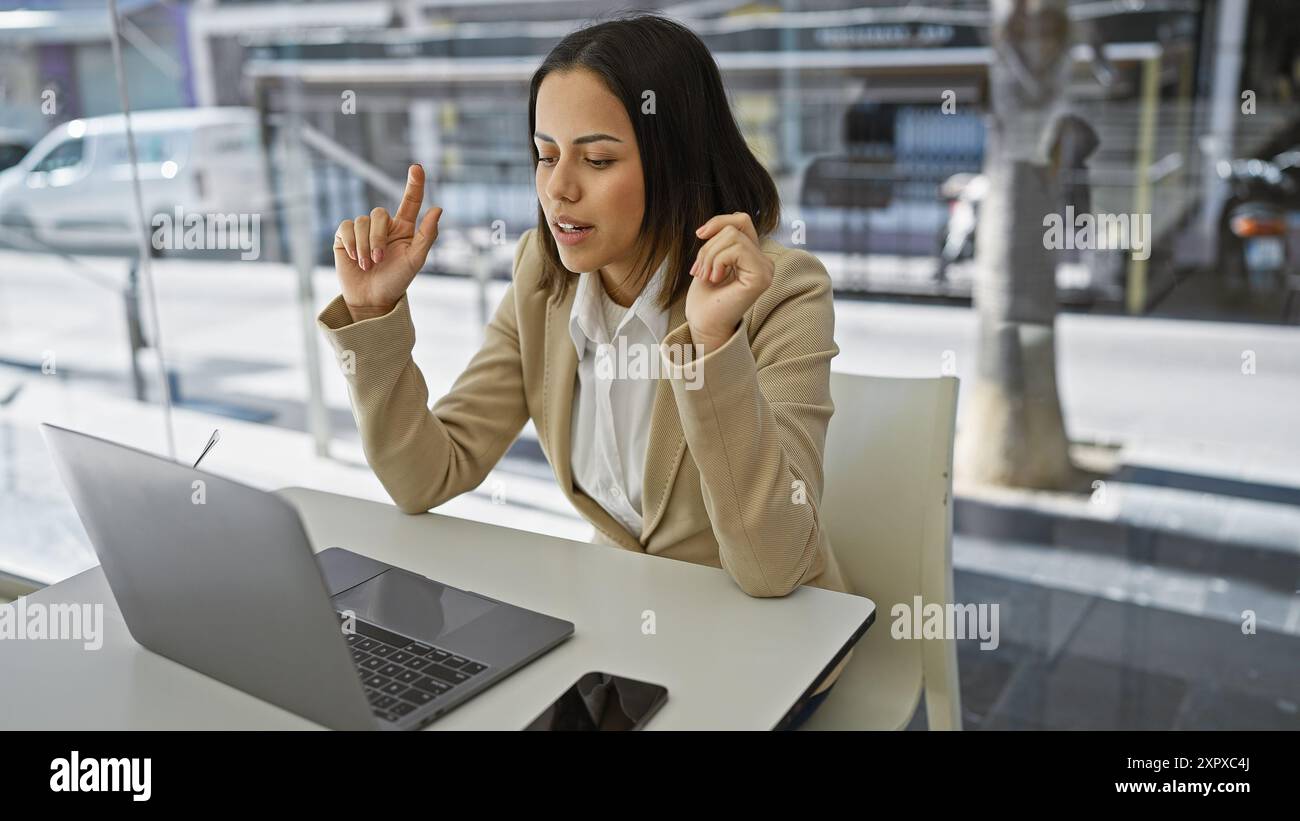 Hispanic woman in a beige blazer gestures while working on a laptop at ...