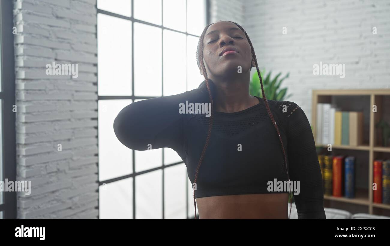 African american woman with braids in pain indoors, holding her neck in ...