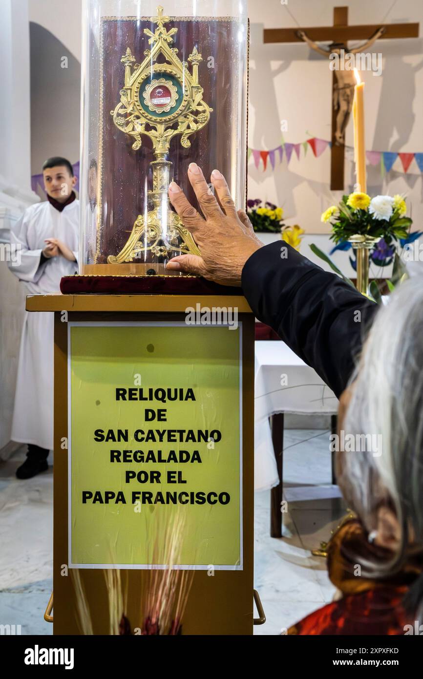 Buenos Aires, Argentina. 07th Aug, 2024. A woman touches the relic of St. Cajetan that was given to the shrine by Pope Francis in 2022. It is a small piece of cloth from the vestment with which the saint celebrated mass. Every August 7, St. Cayetano, the saint of bread and work, is celebrated. Millions of devotees congregate in the different sanctuaries throughout the country to ask for his intercession and thank him for the favors received. The lines begin days before the celebration and once the doors open people wait up to 7 hours to enter. Credit: SOPA Images Limited/Alamy Live News Stock Photo