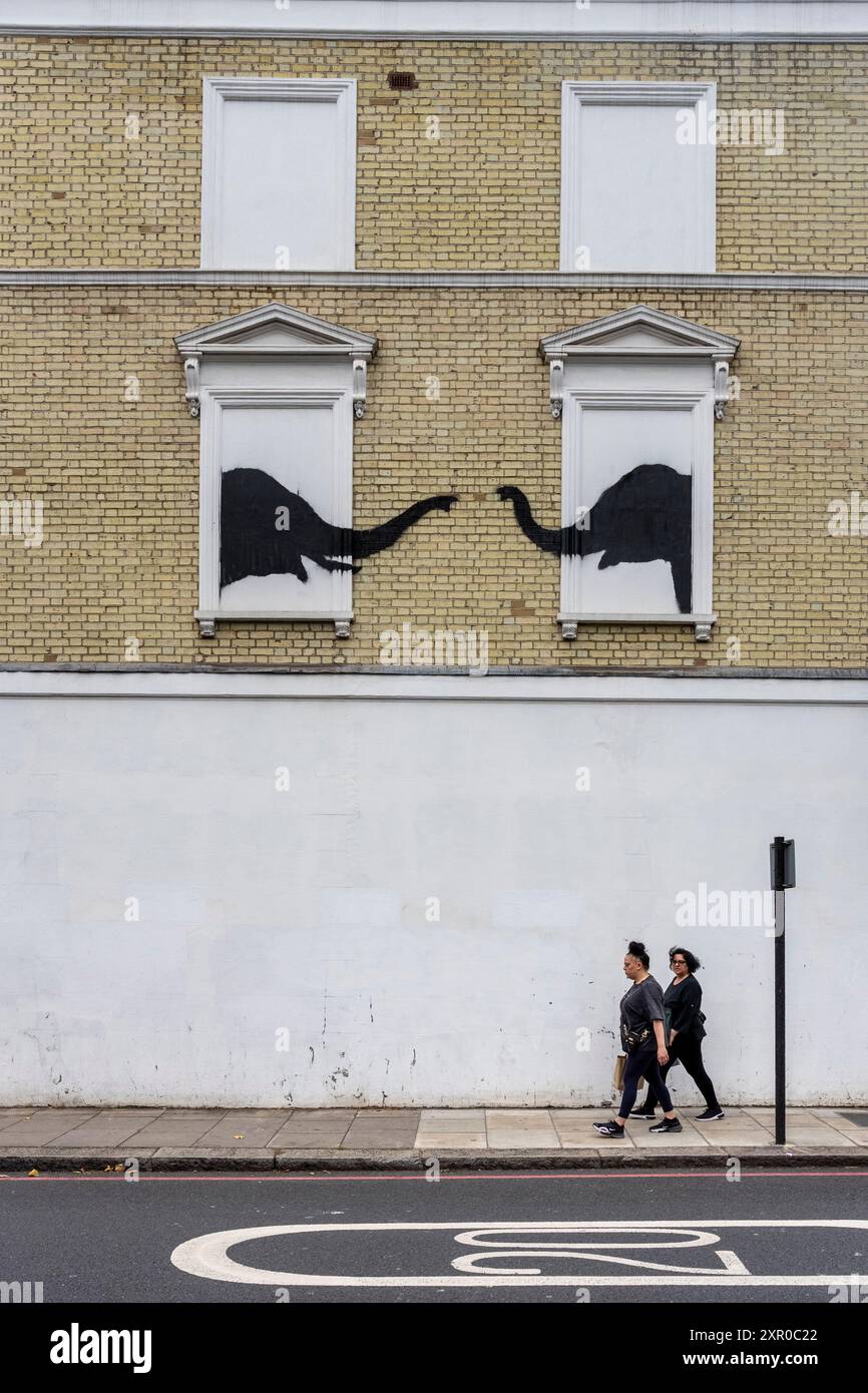 London, UK.  8 August 2024.  People pass an artwork by Banksy depicting a pair of elephants on the side of a building near Chelsea.  In the last week, new works by the artist have appeared daily in the capital with an animal theme.  So far the trail includes a mountain goat, two elephants and three monkeys. A fourth work, depicting a howling wolf painted on a satellite dish in Peckham, has already been stolen shortly after being revealed today.  Credit: Stephen Chung / Alamy Live News Stock Photo