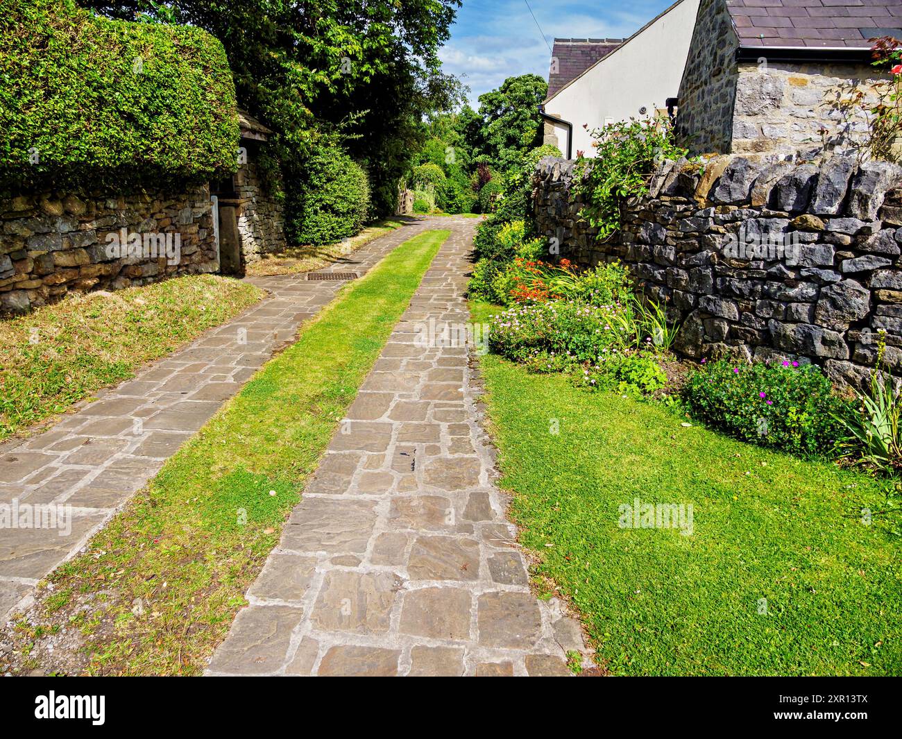 Charming narrow cobblestone path lined with lush greenery and historic stone walls in a quaint village setting. Stock Photo