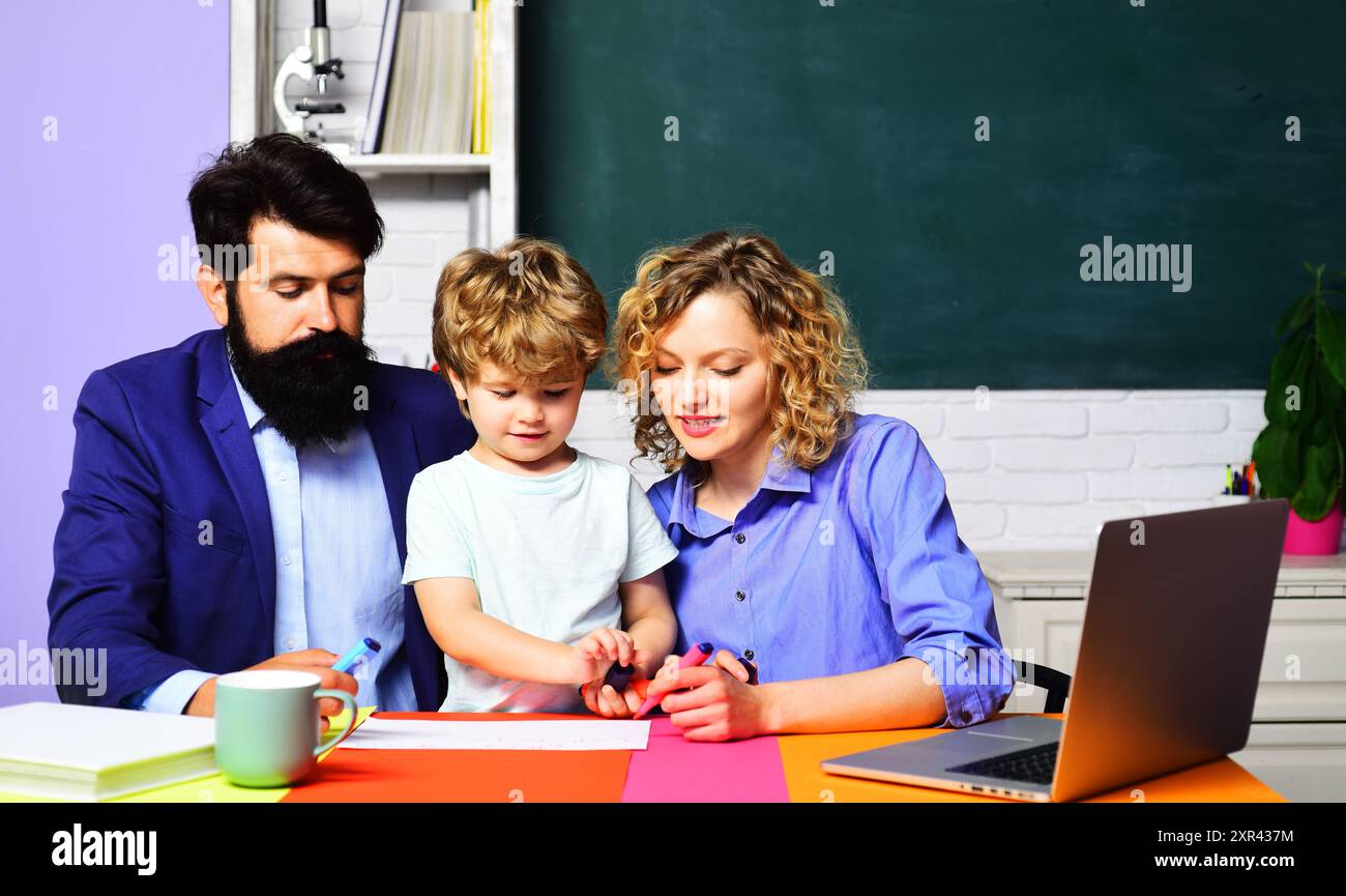 Cute boy from elementary school doing schoolwork with male and female teachers. Private lesson. Child from primary school make homework with father an Stock Photo