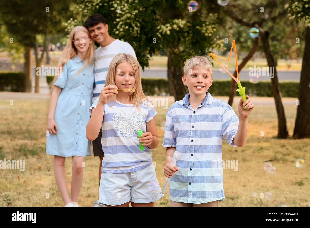 Happy couple hugging and their cute children blowing soap bubbles in ...