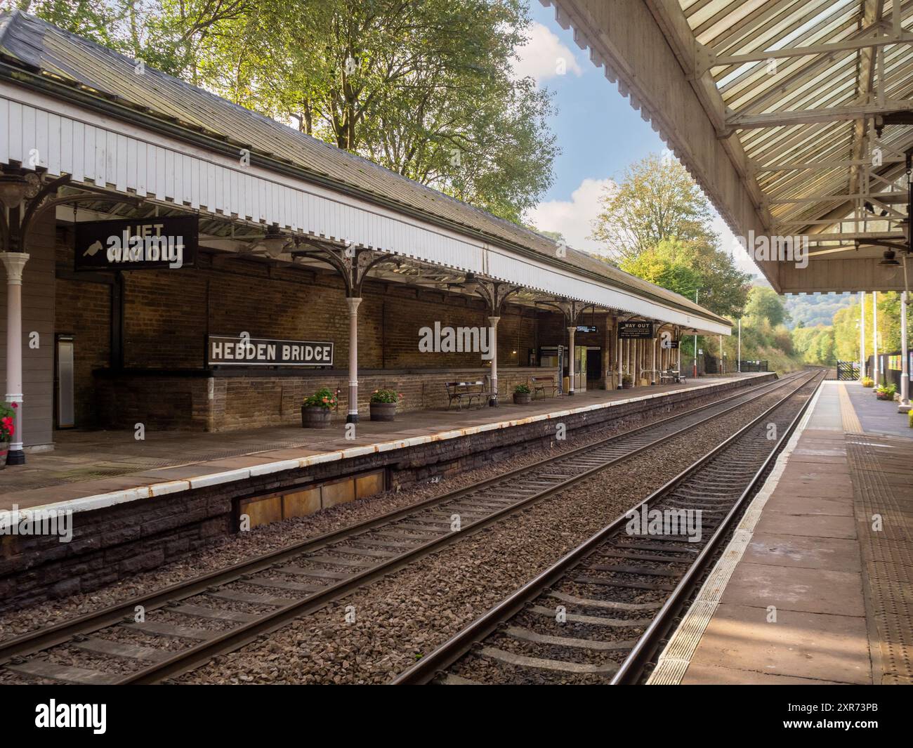 Hebden Bridge Victorian station platform, covered by a canopy, with rail tracks alongside on a warm, sunny day. Stock Photo