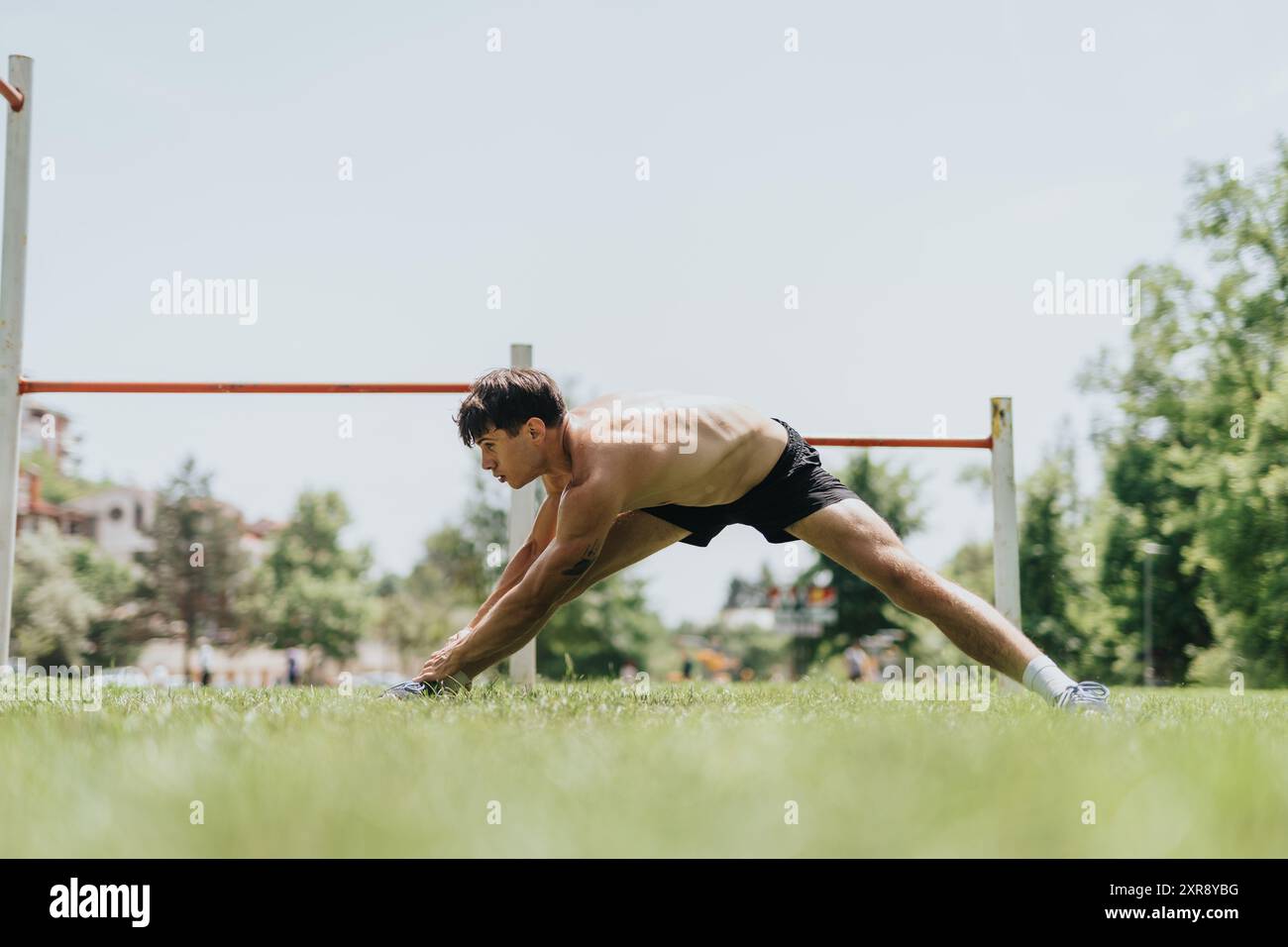 Fit man exercising outdoors, performing stretching routine in nature Stock Photo