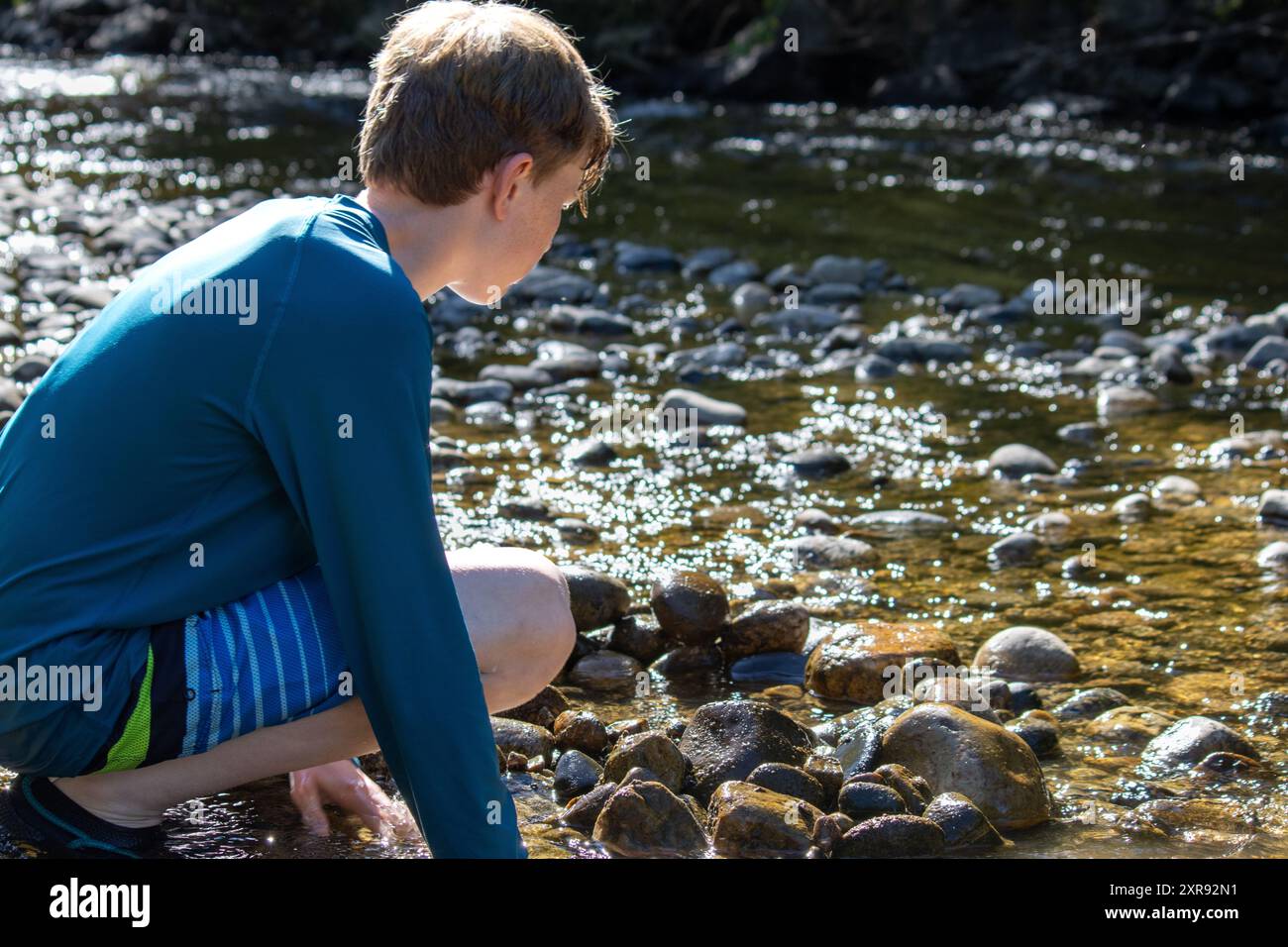 Boy crouching by a creek, playing with the rocks and water Stock Photo ...