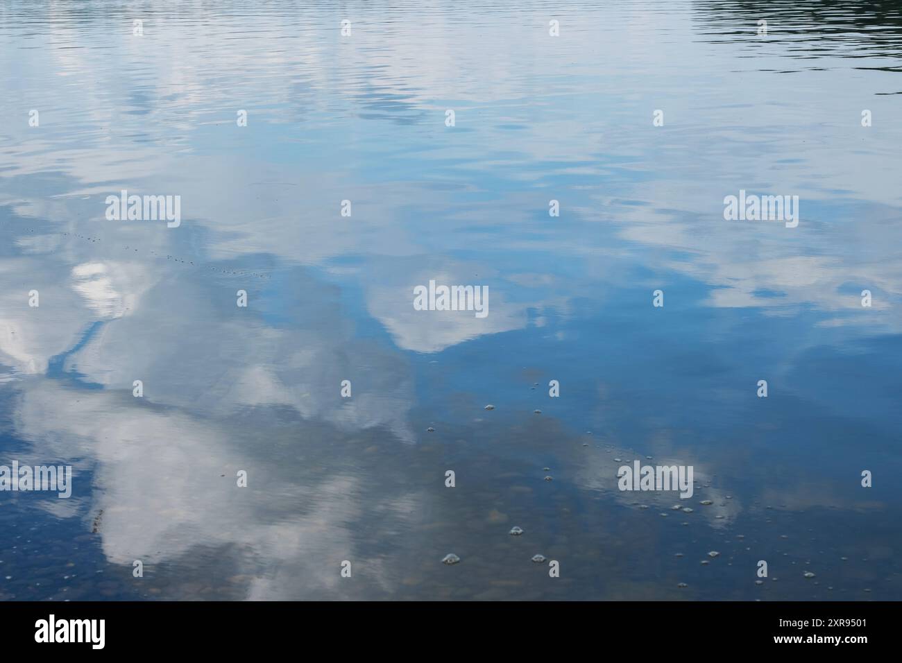 Reflection of sky and clouds on calm water surface creating serene ...