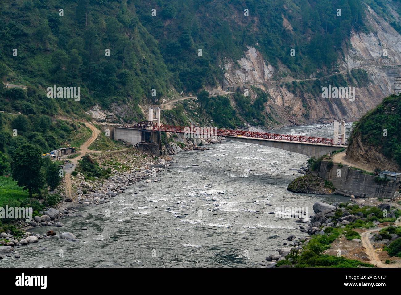 A long bridge spanning between two hills with the Ravi River flowing underneath in the Chamba District of Himachal Pradesh, India. Stock Photo