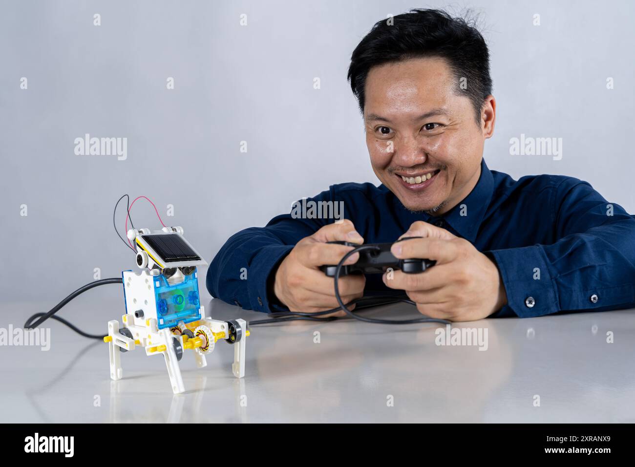 Asian man is building a robot project in his home. Robots control science lessons and coding, developing learning innovations Close-up view Stock Photo