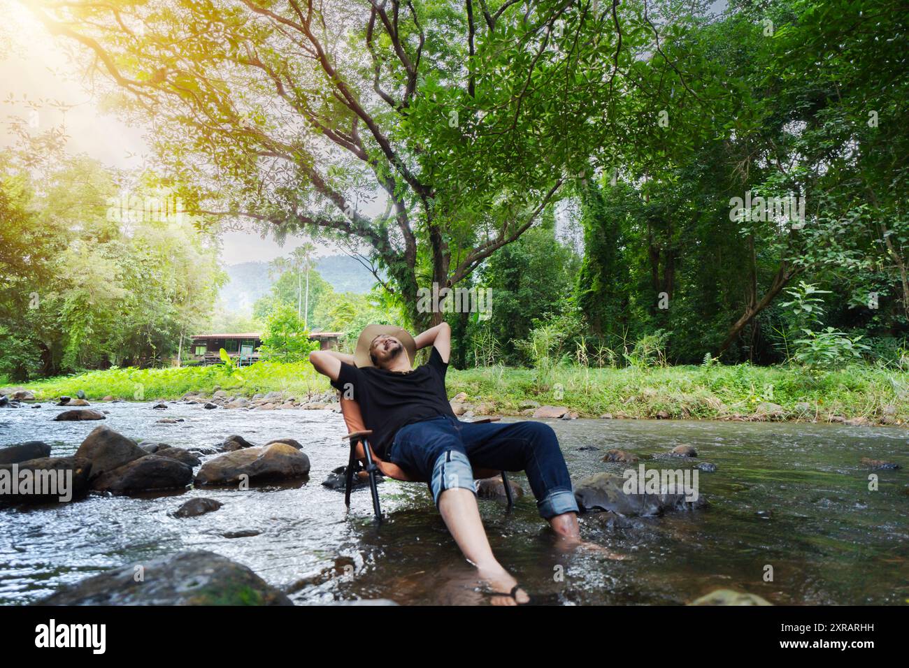 Mature bearded man sits on a chair in the middle of the stream and happily writes at the weekend, smiling faces rejoice in the rest. Stock Photo