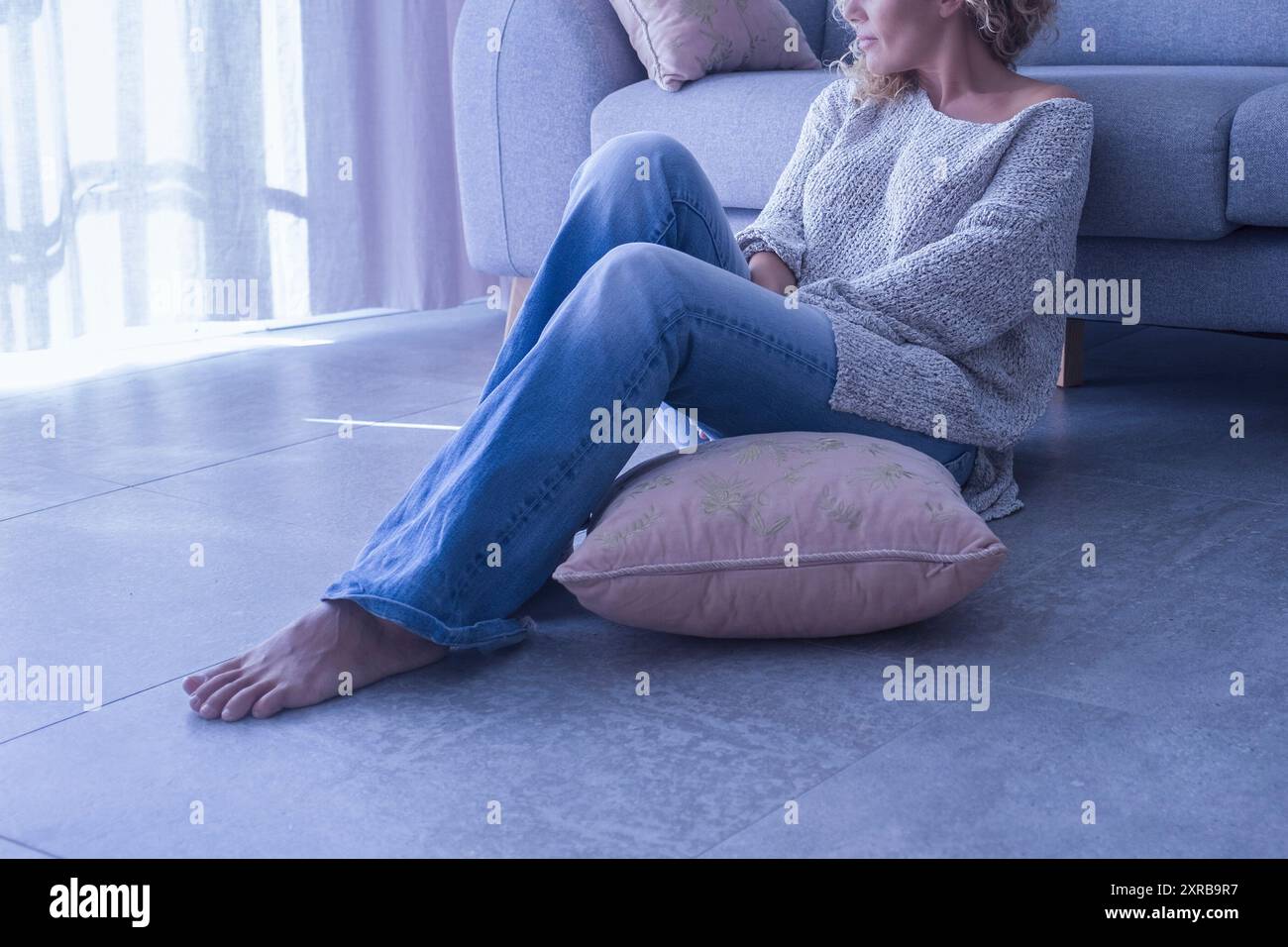 Thoughtful woman sitting on the floor at home looking out the window ...