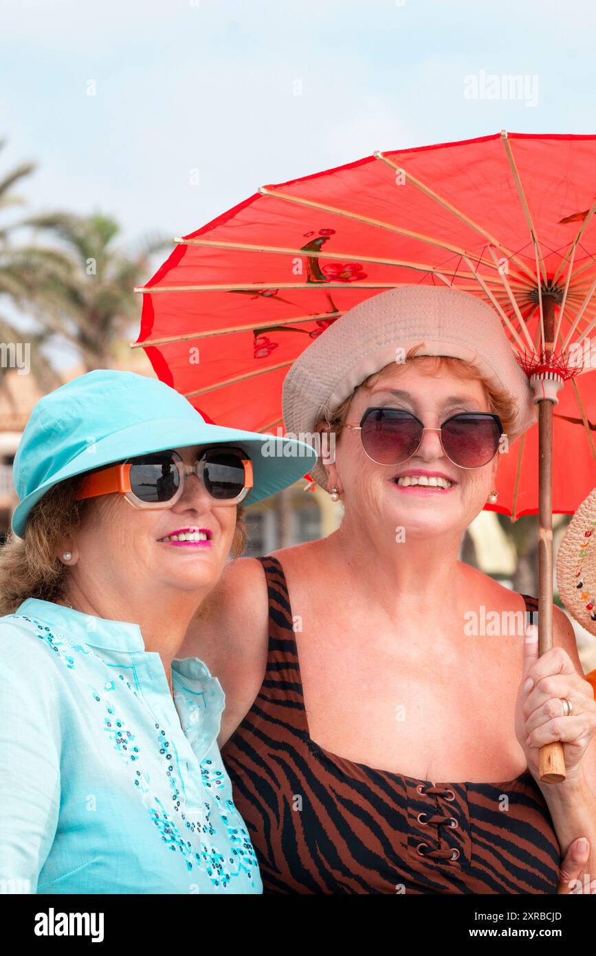 Group mature women wearing beach hats and smiling while standing on a tropical beach. Older