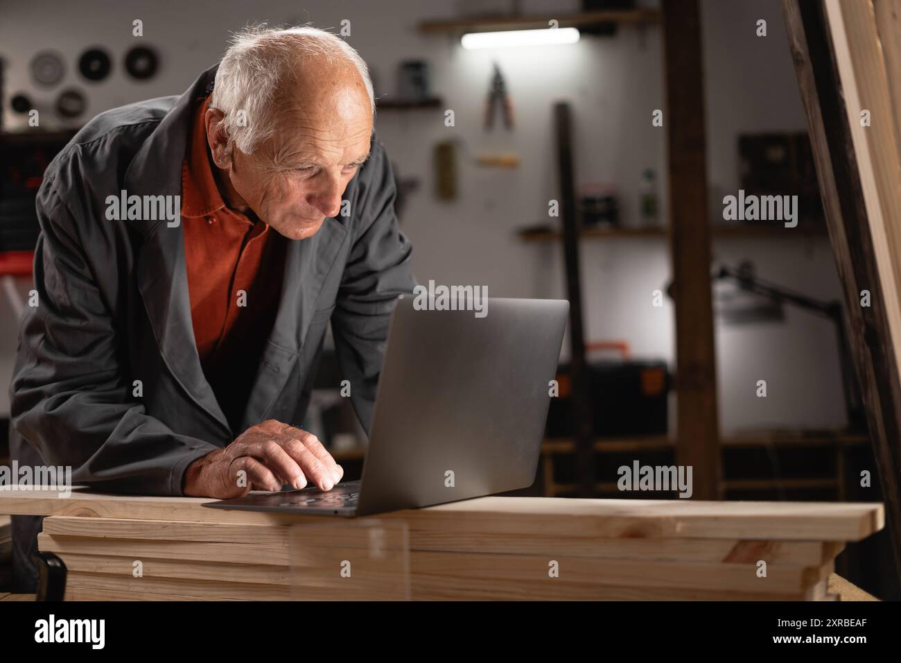 Elderly Man Using Laptop in His Small Business Workshop Stock Photo