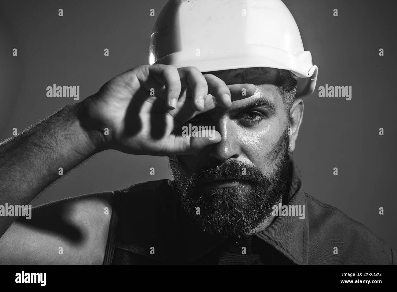 Tired builder in safety helmet. Hard work at construction site. Fatigued industrial worker wipes sweat from forehead. Heavy profession. Male architect Stock Photo