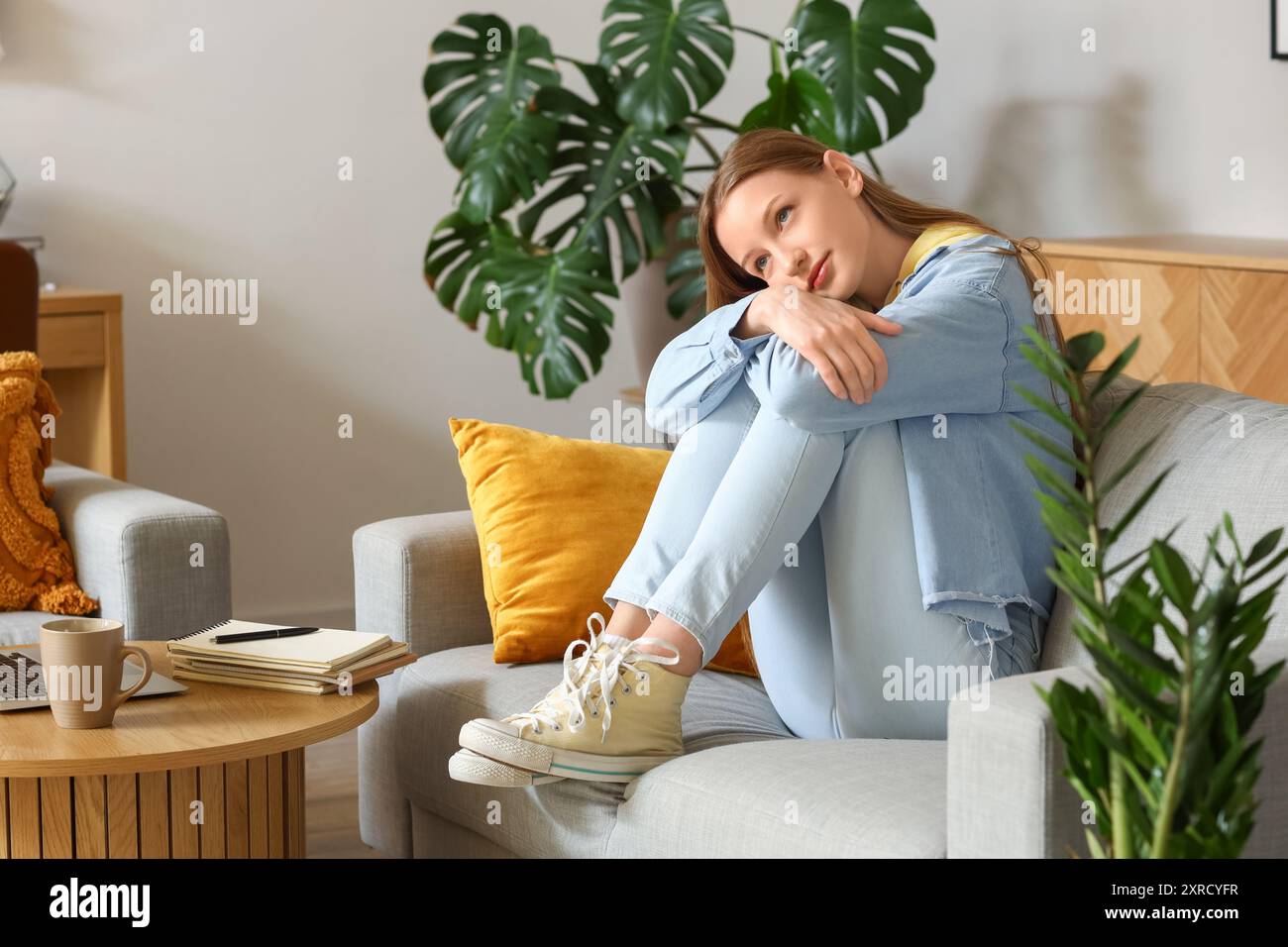 Thoughtful teenage girl sitting on sofa at home Stock Photo - Alamy