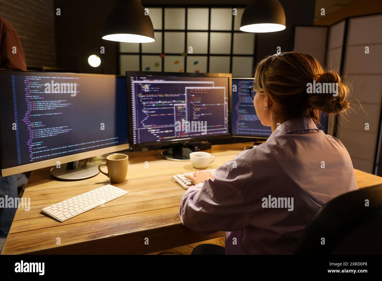 Female programmer working with computer in office at night, back view ...