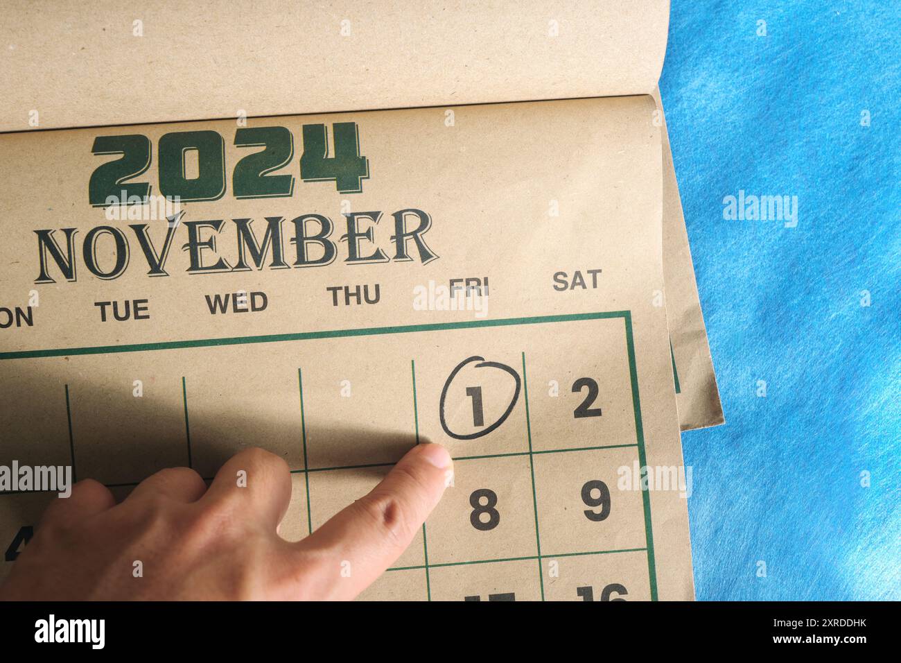 Hand pointing on November 1 2024 date on calendar flat lay in blue background. First day of the month reminder. Stock Photo