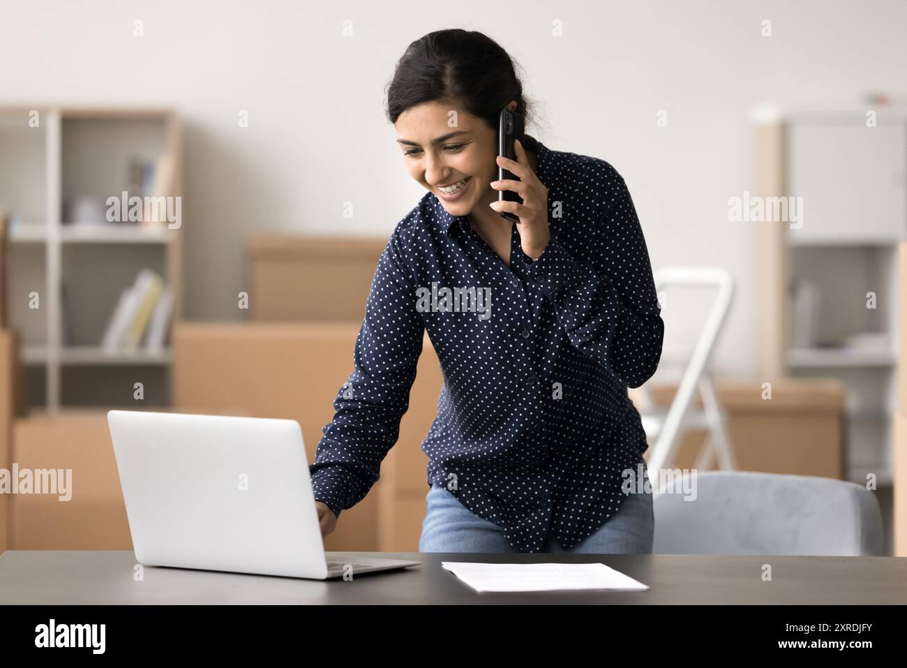 Indian female, warehouse worker using laptop while talking on phone Stock Photo