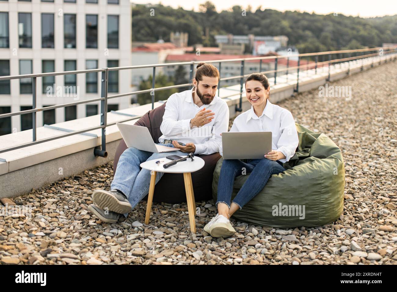 Two colleagues working on laptops outdoors on a rooftop Stock Photo