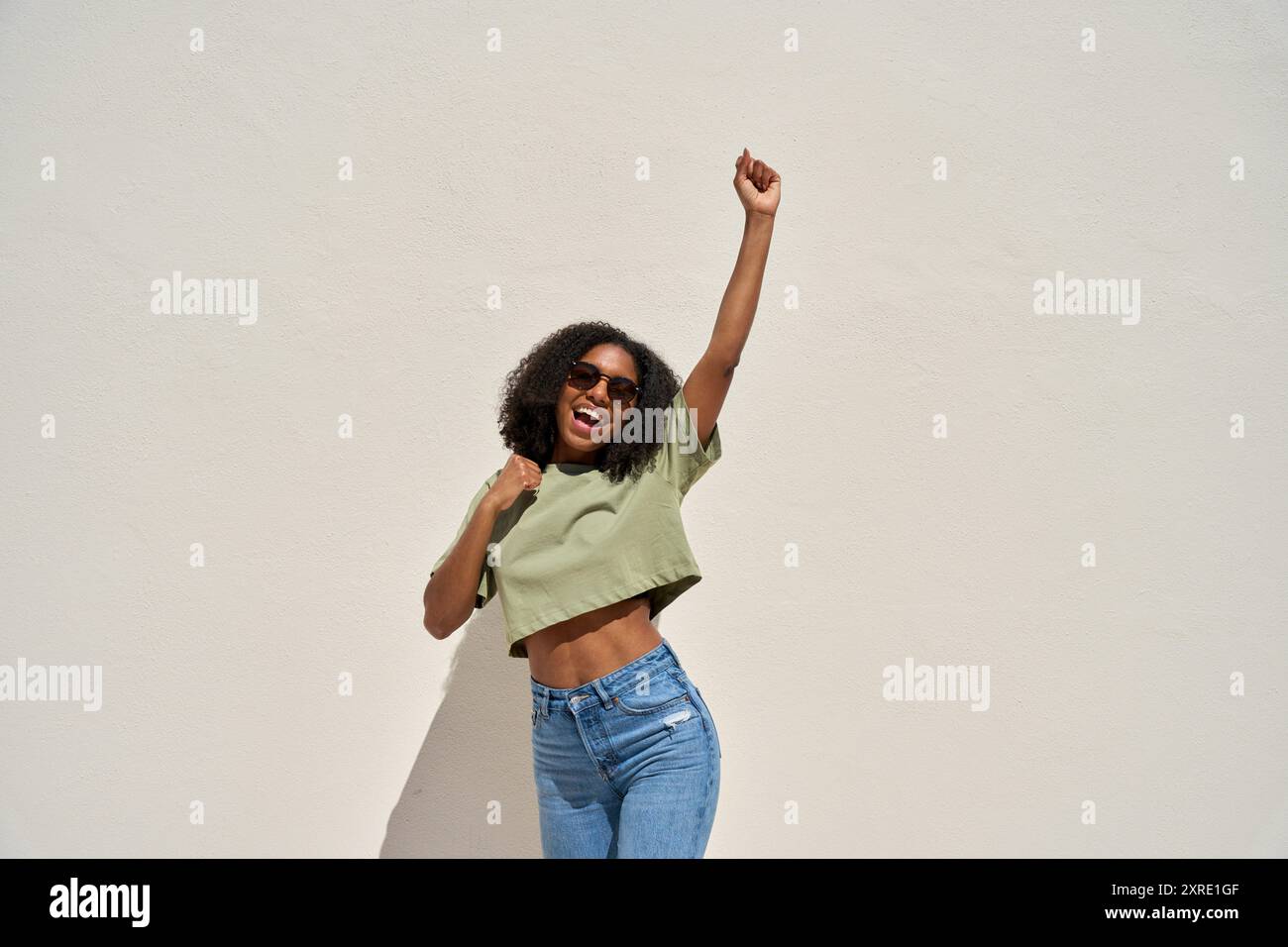 Happy young African American woman winner dancing at white background ...
