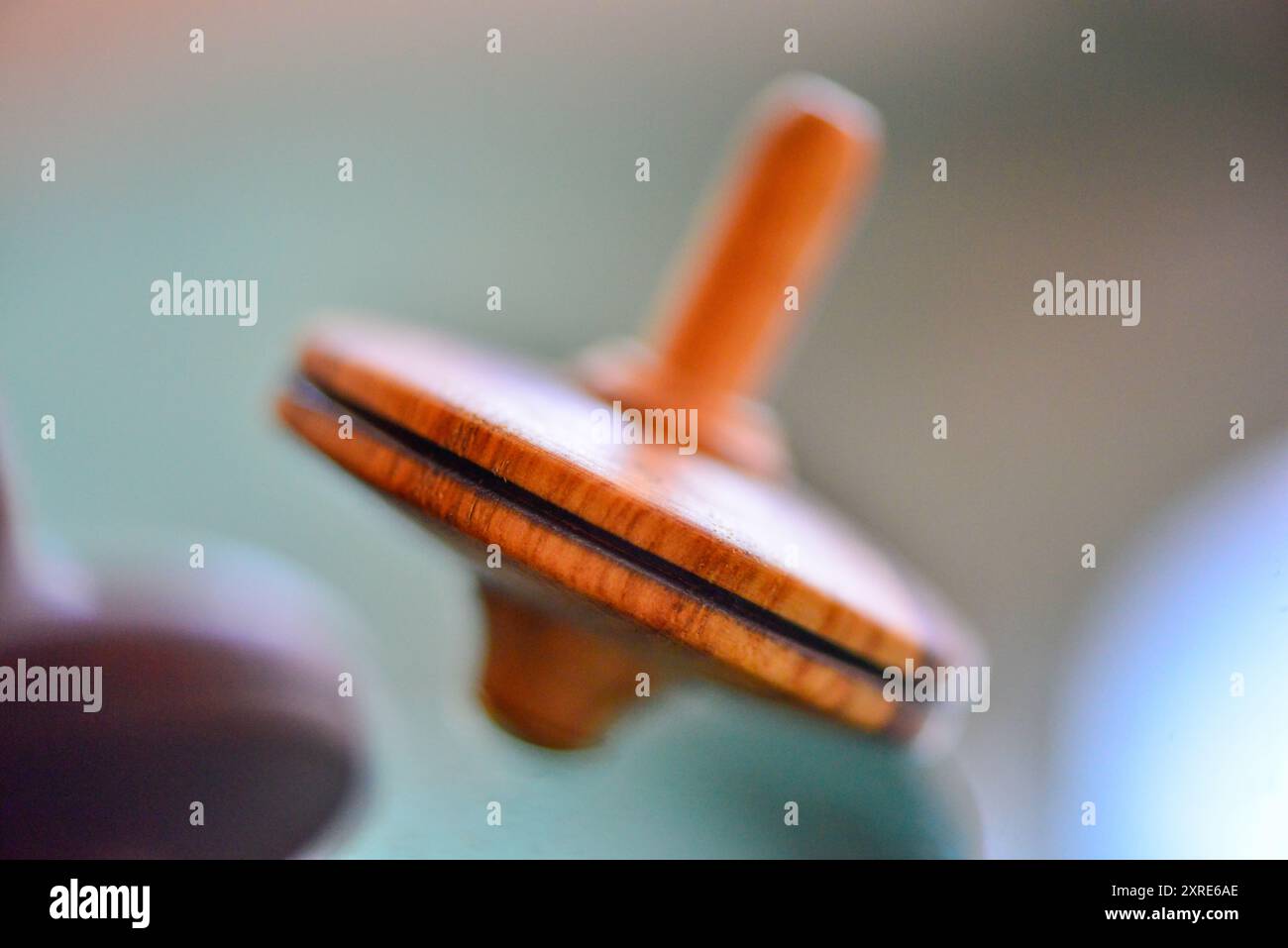 A macro photo of a wooden teetotum spinning and standing on a glass surface, showcasing its intricate craftsmanship and smooth, reflective surface. Stock Photo