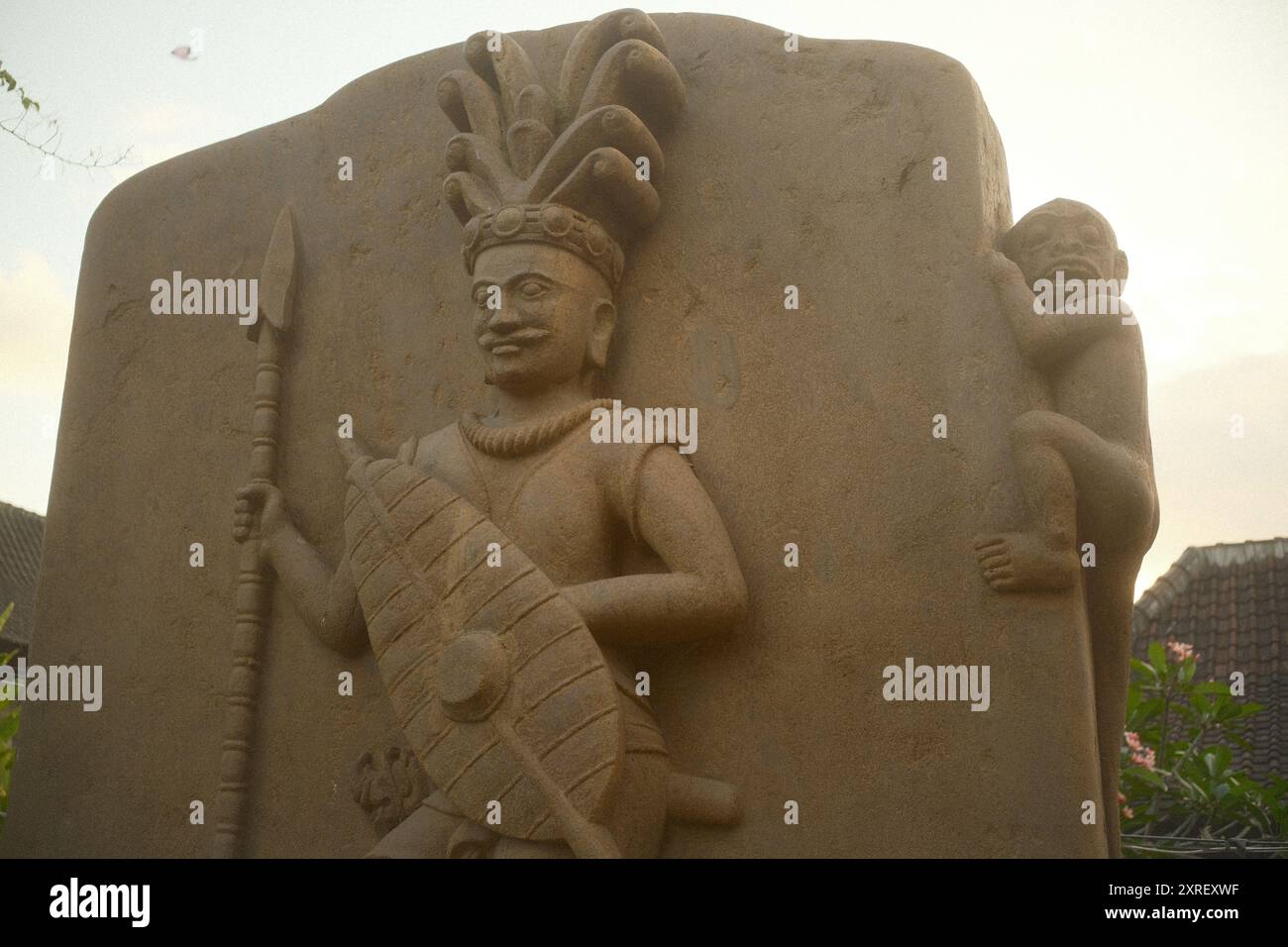 Tabanan, Bali, Indonesia - August 9, 2024: An carved stone art and craft sculpture of a indigenous tribesman in traditional attire with traditional we Stock Photo
