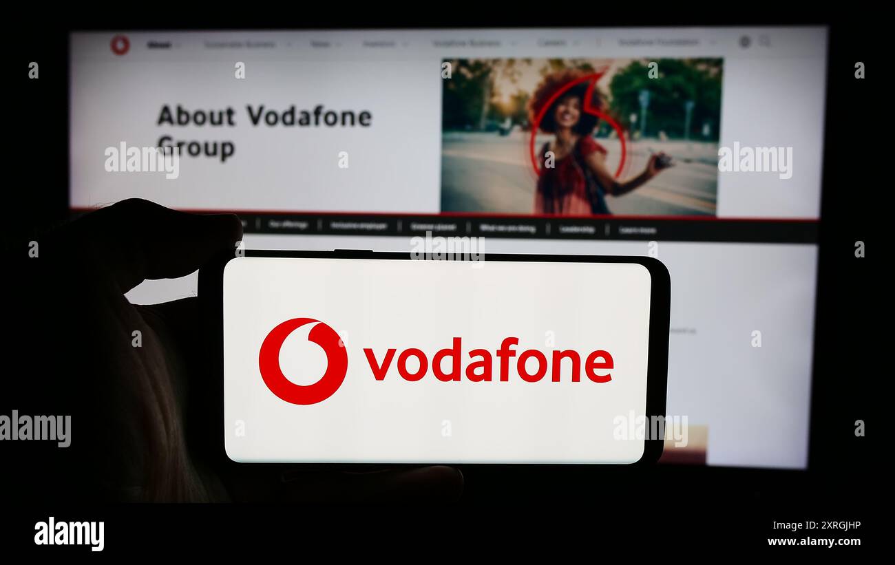 Person holding cellphone with logo of British telecommunications company Vodafone Group plc in front of business webpage. Focus on phone display. Stock Photo