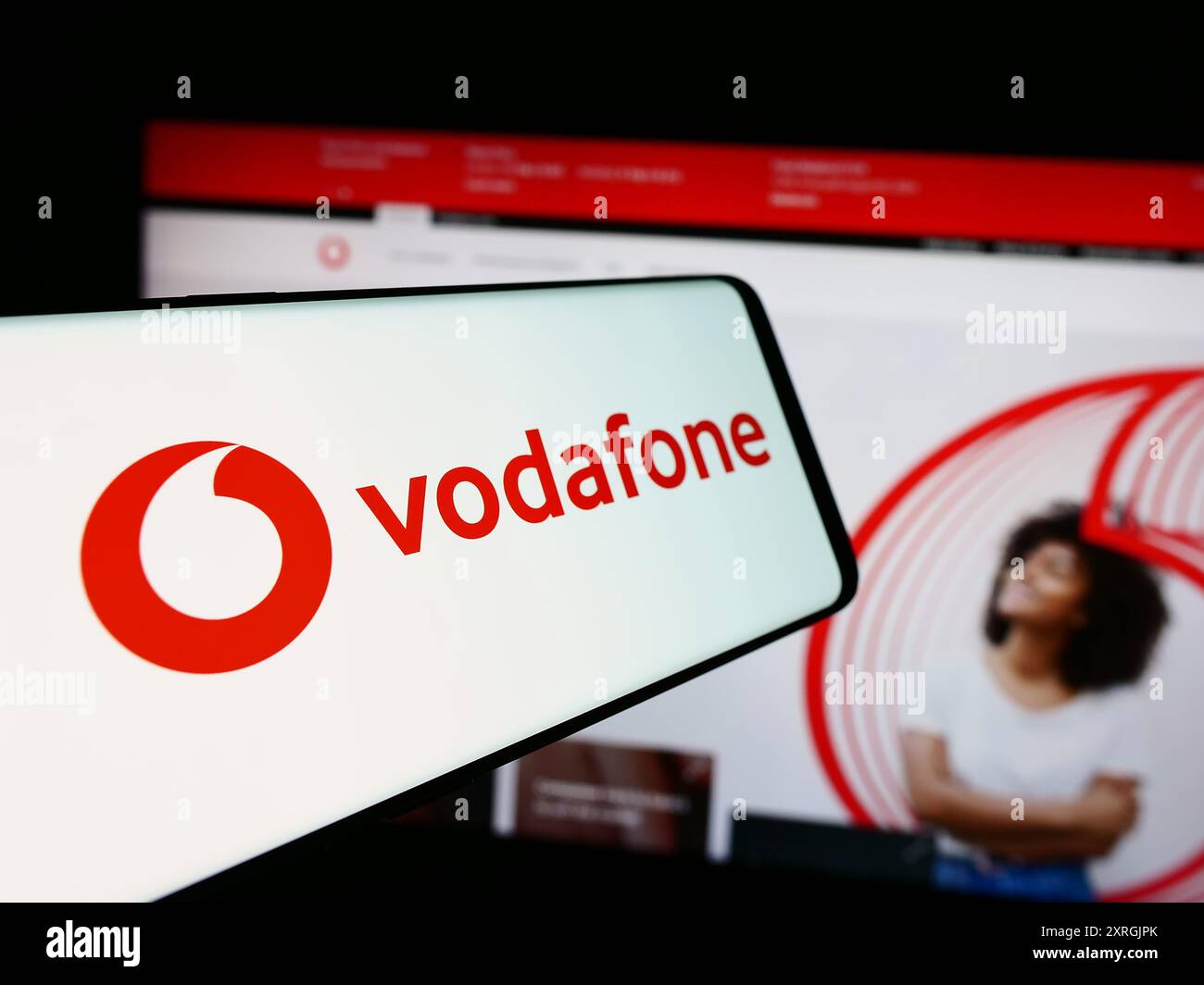 Cellphone with logo of British telecommunications company Vodafone Group plc in front of business website. Focus on center-left of phone display. Stock Photo