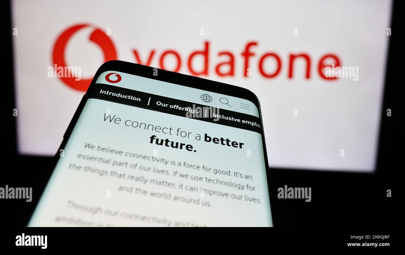 Mobile phone with website of British telecommunications company Vodafone Group plc in front of business logo. Focus on top-left of phone display. Stock Photo