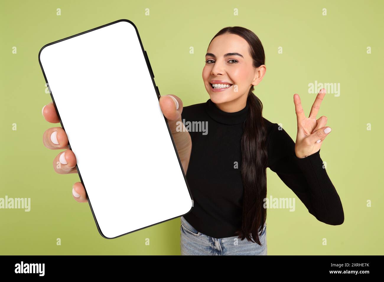 Happy woman showing mobile phone with blank screen on light green ...