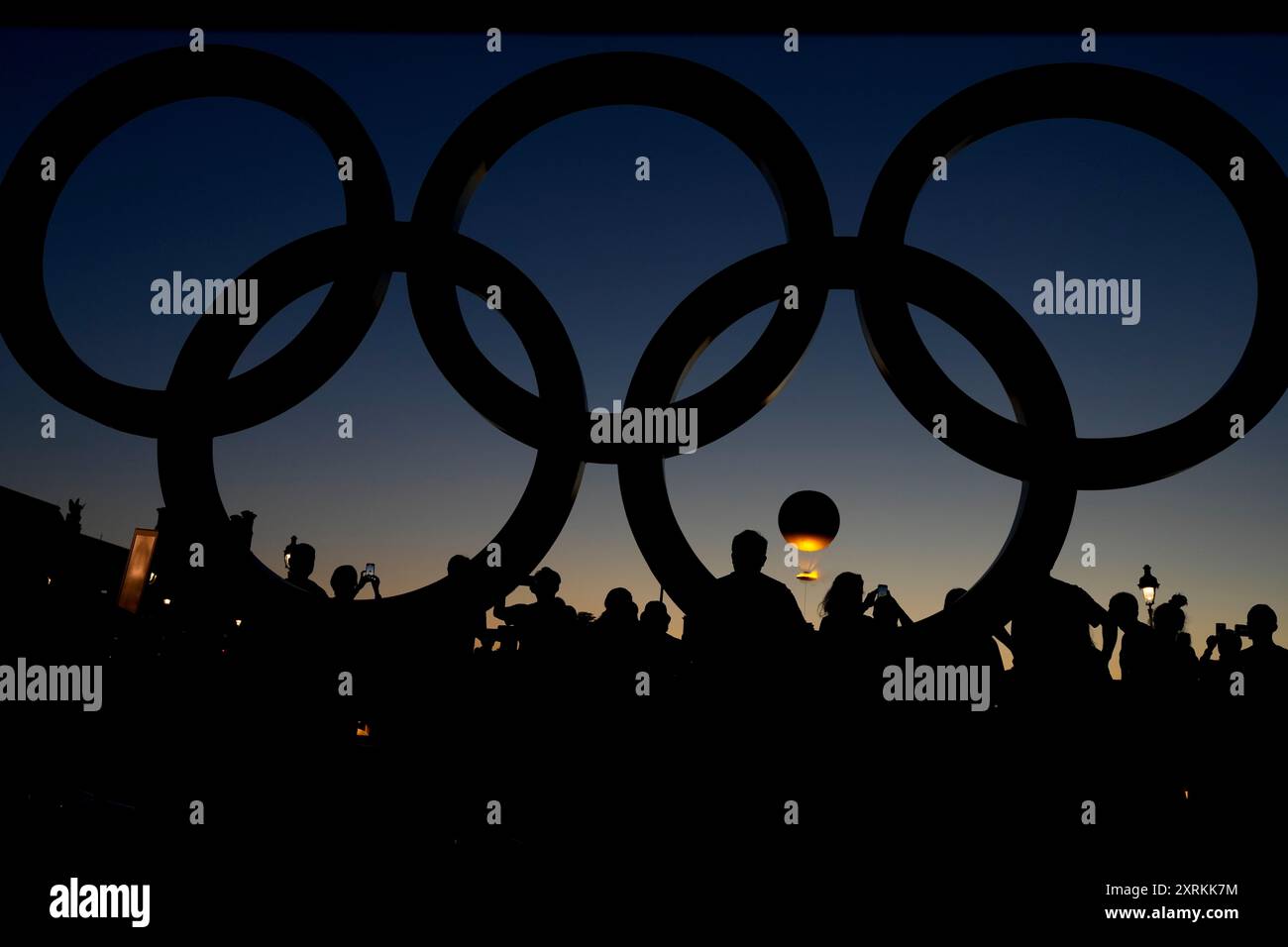 People watch the cauldron rise at sunset by the Olympic rings during ...