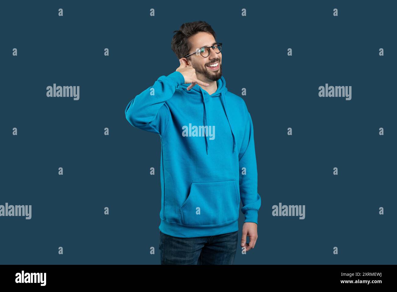 Friendly Man In Blue Hoodie Smiling While Making Call Gesture Stock Photo