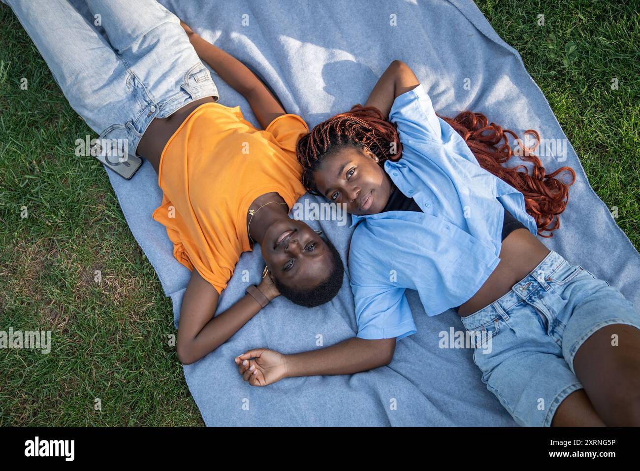 Relaxed cheerful black couple of girls friends lounging, lying on blanket on grass in park Stock Photo