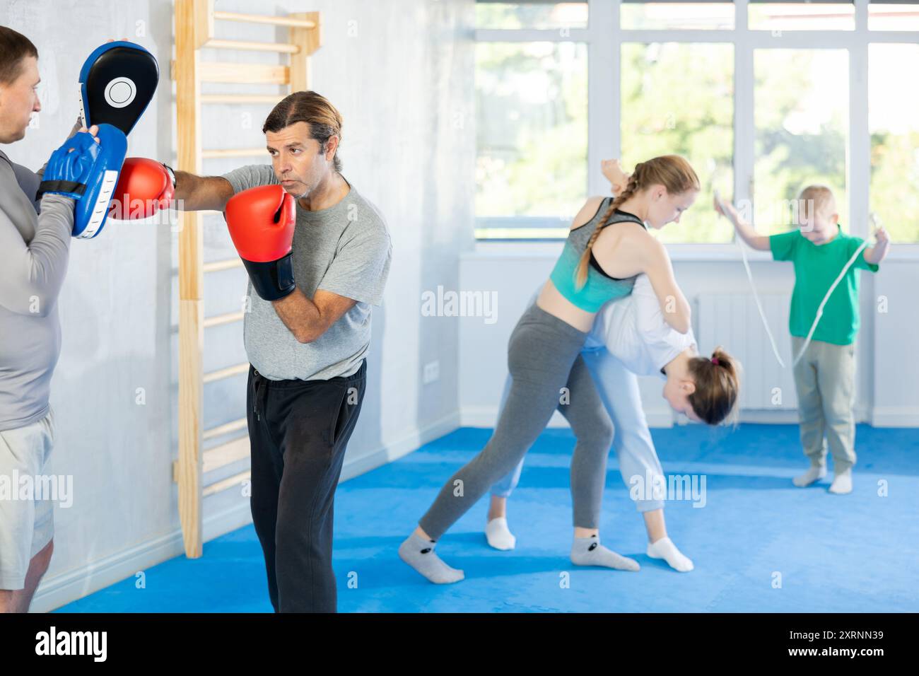 Focused man in boxing gloves practices punches with man in mitts in gym Stock Photo