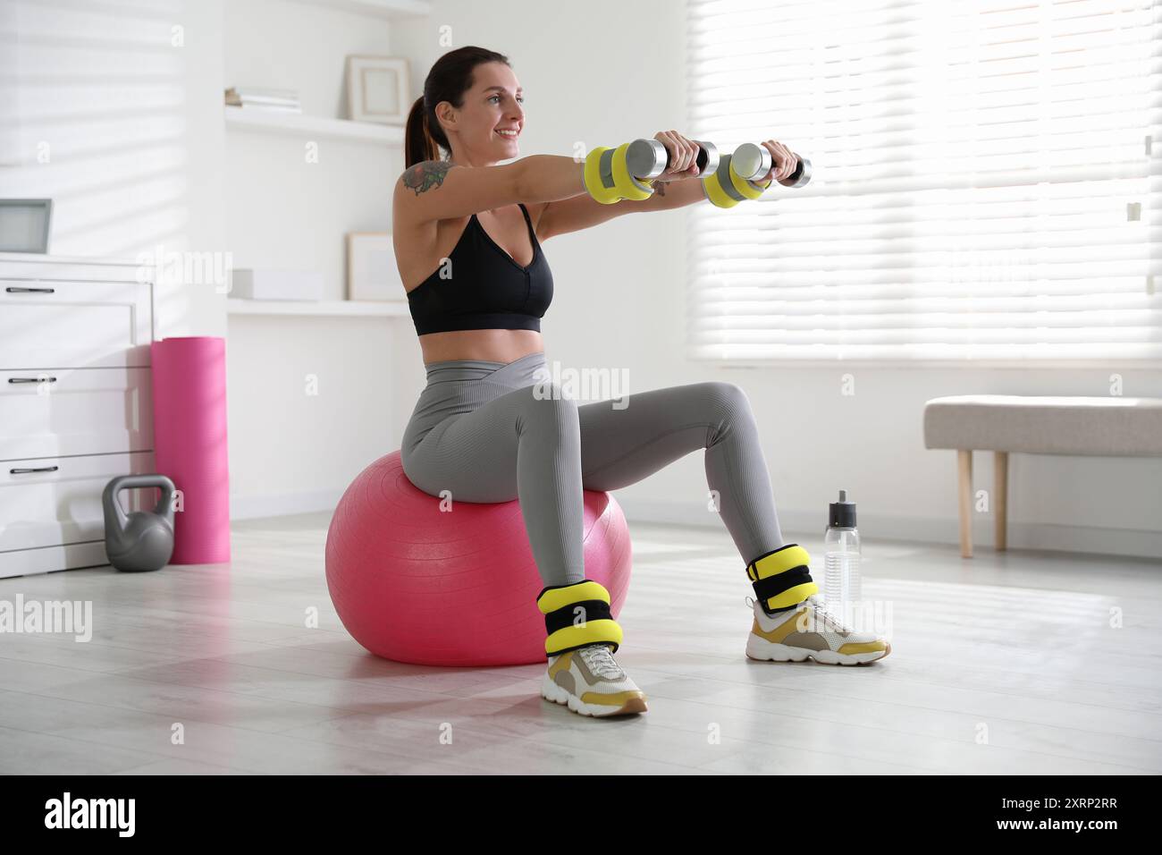 Beautiful woman with ankle weights and dumbbells training on fitness ball indoors Stock Photo Alamy