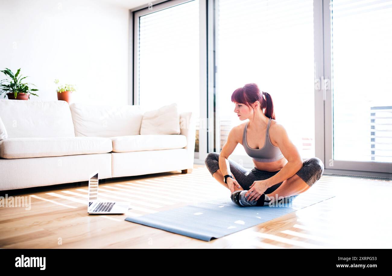 Online workout program with trainer. Beautiful redhead woman exercising in living room looking at notebook Stock Photo Alamy