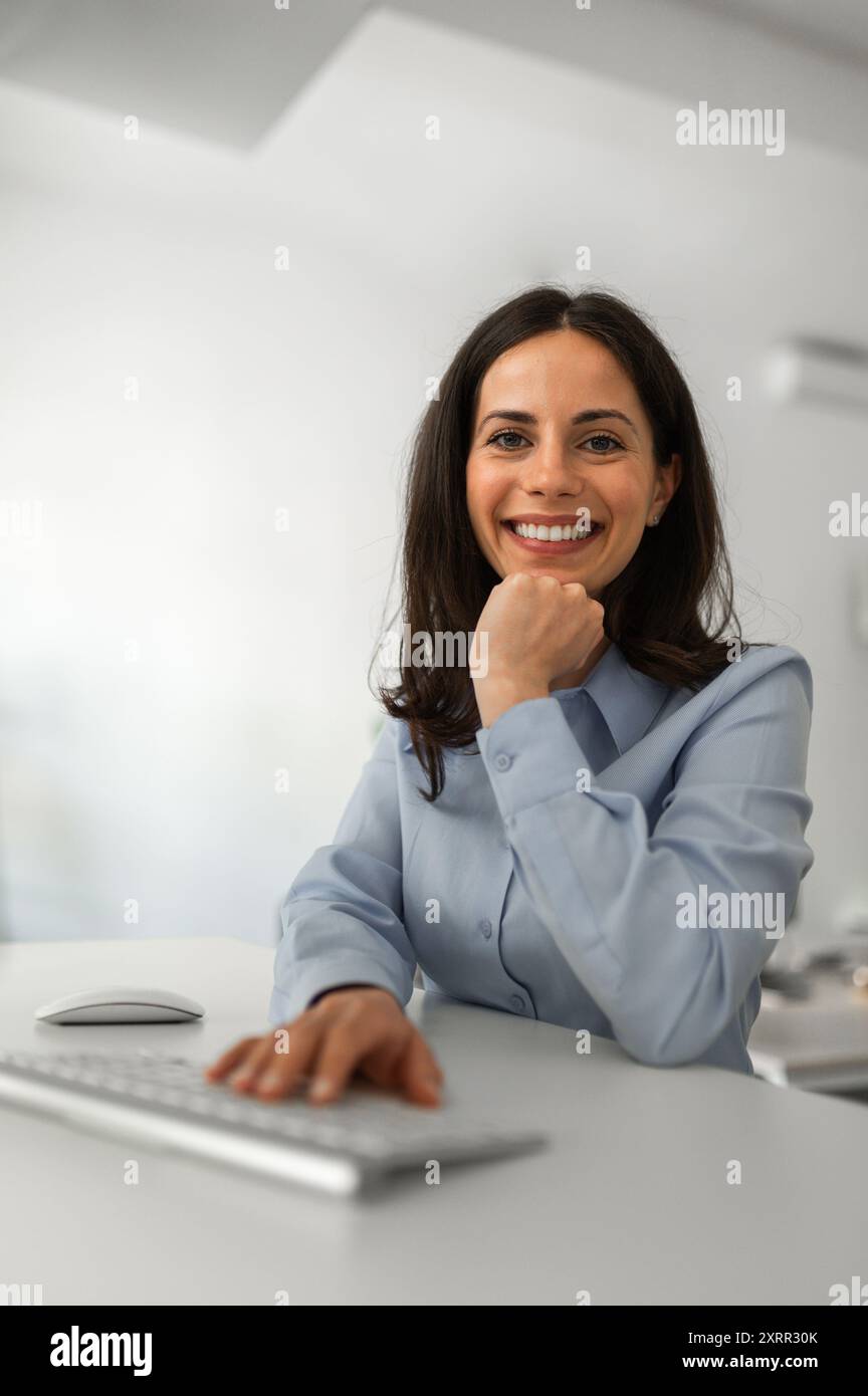 Portrait of young cheerful woman sitting at her office desk Stock Photo