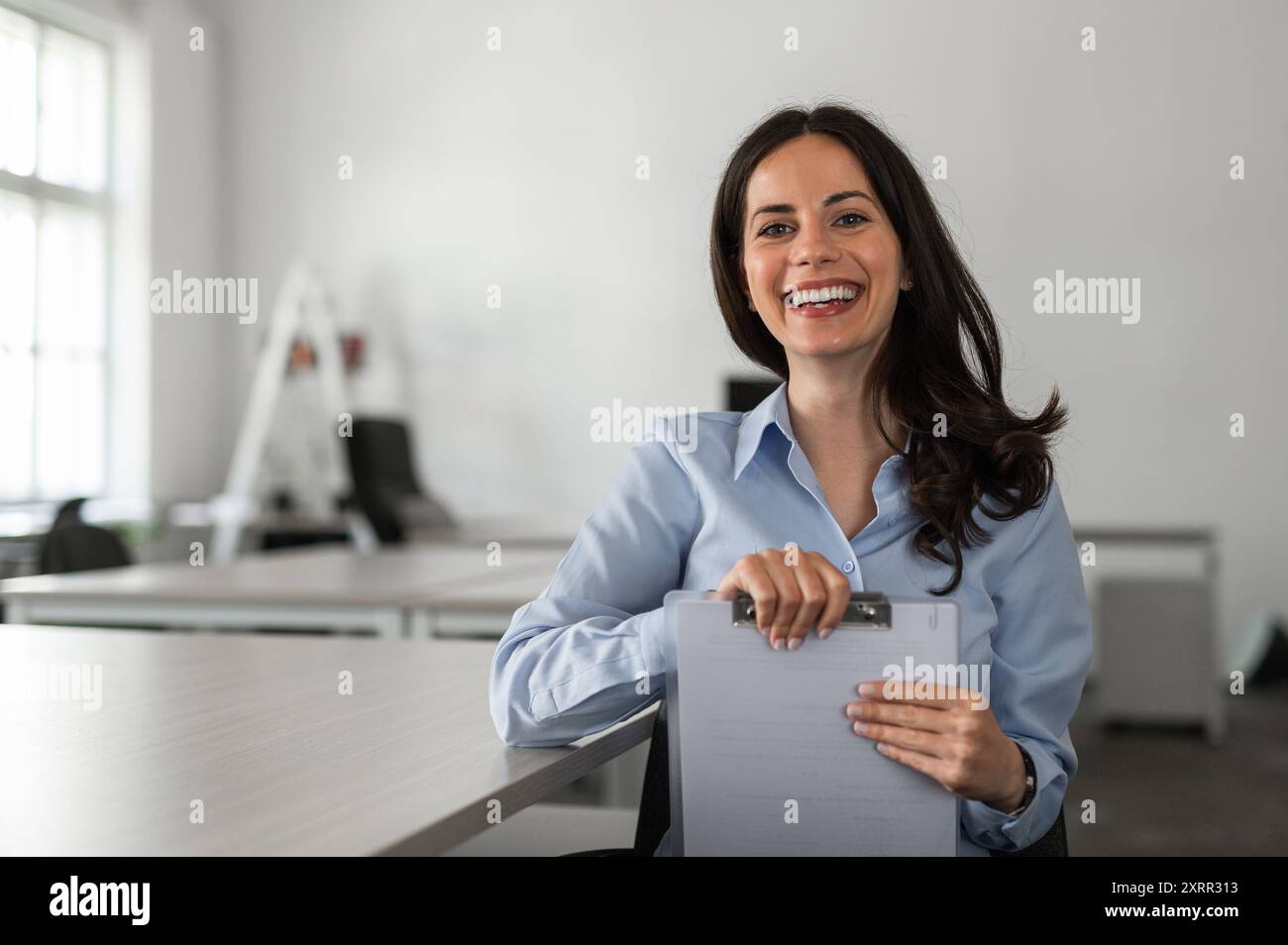 Young and cheerful employee at her desk holding documents Stock Photo