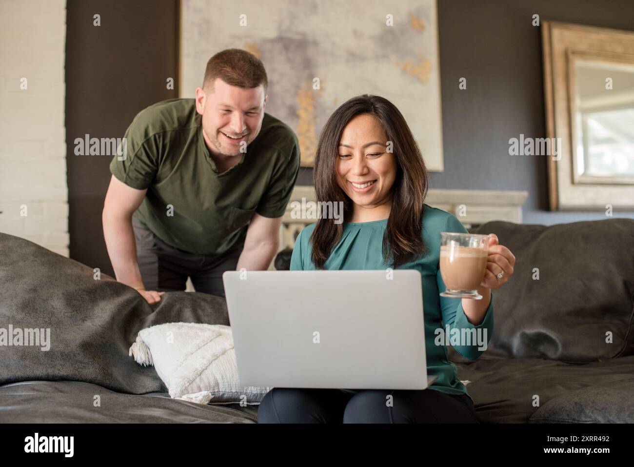Couple smiling at laptop together sitting on couch Stock Photo - Alamy