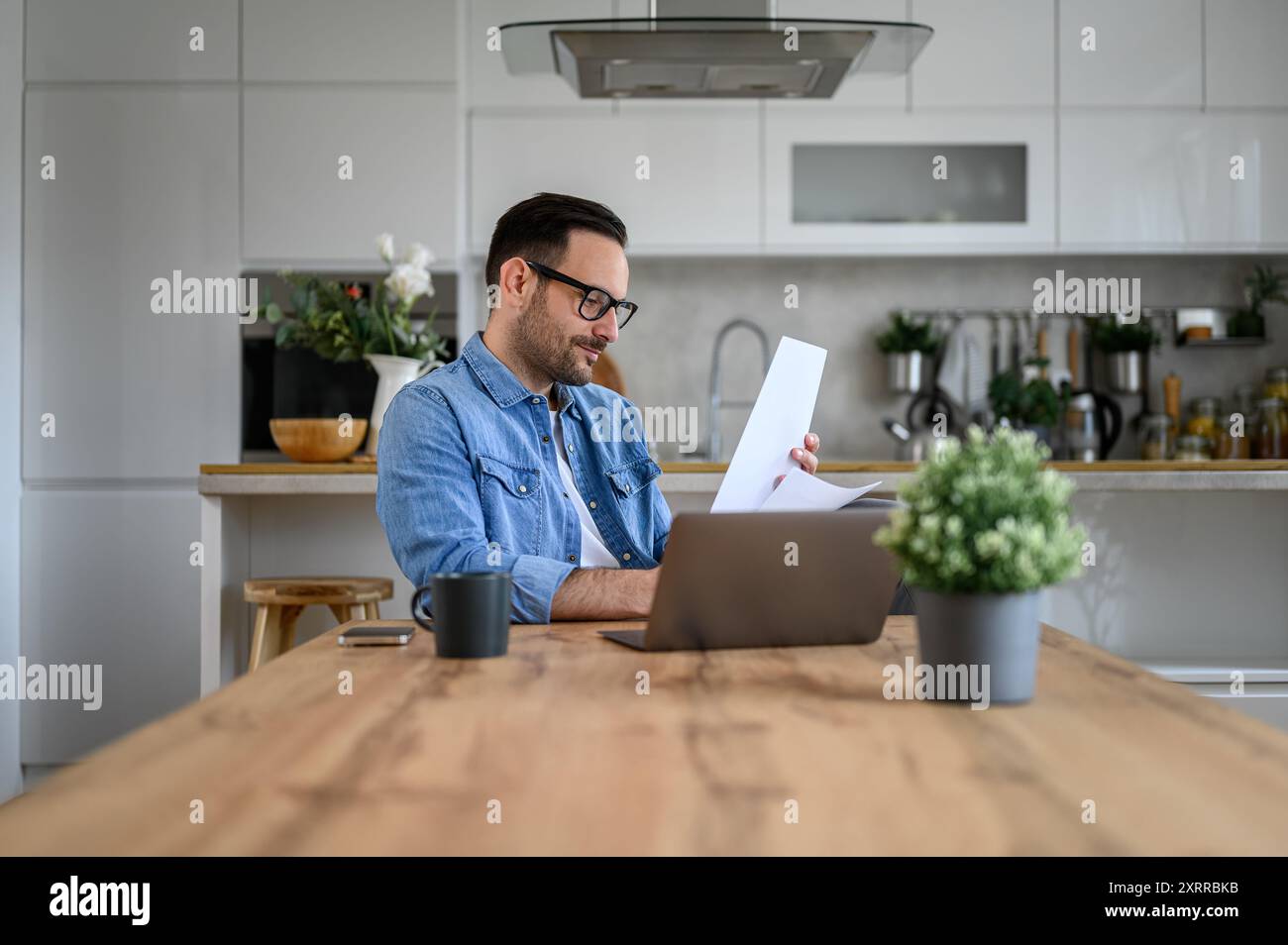 Young entrepreneur with laptop on desk analyzing financial report while working from home office Stock Photo