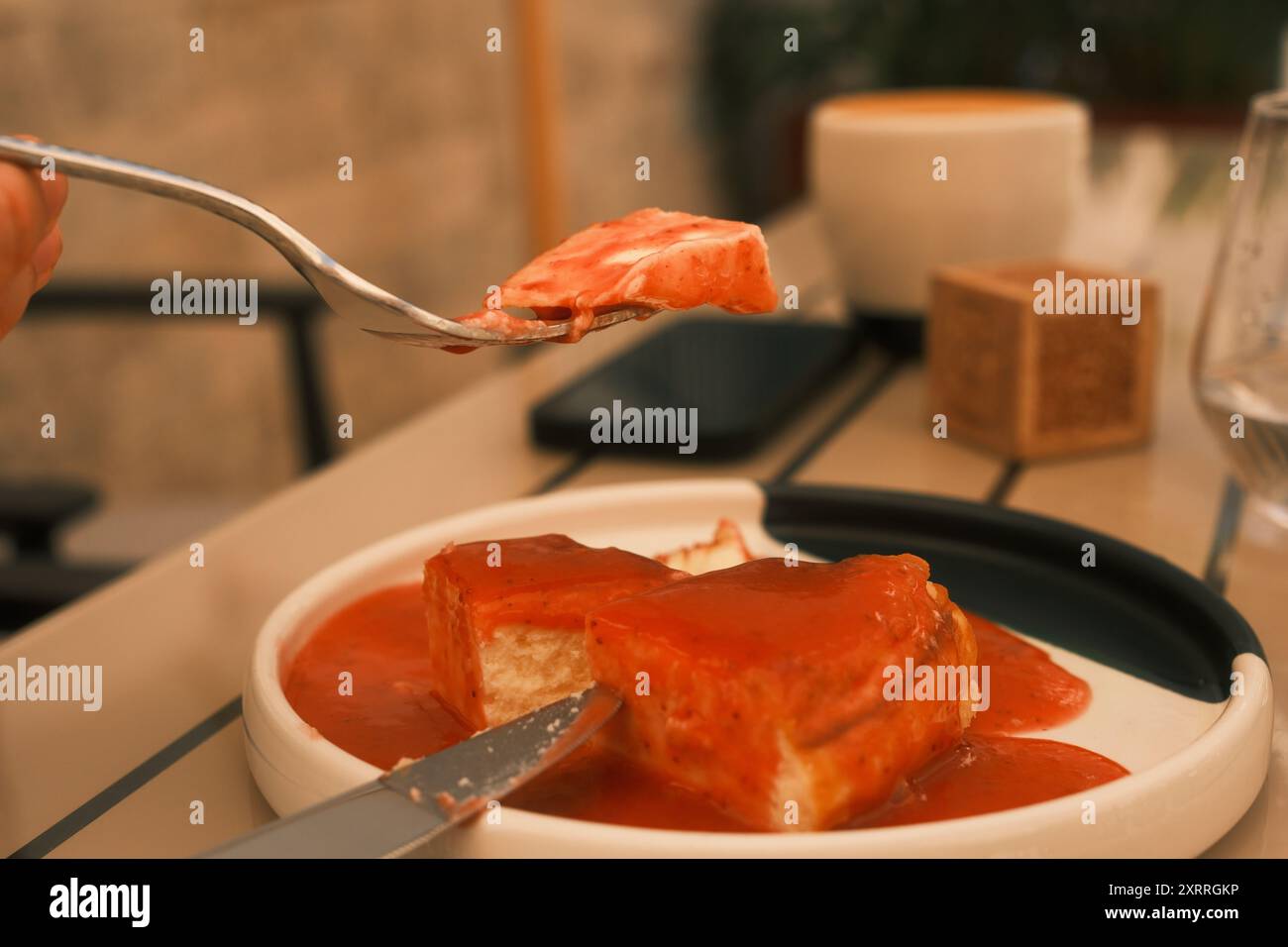 A person is eating a piece of cake with a fork. The cake is covered in a red strawberry sauce Stock Photo