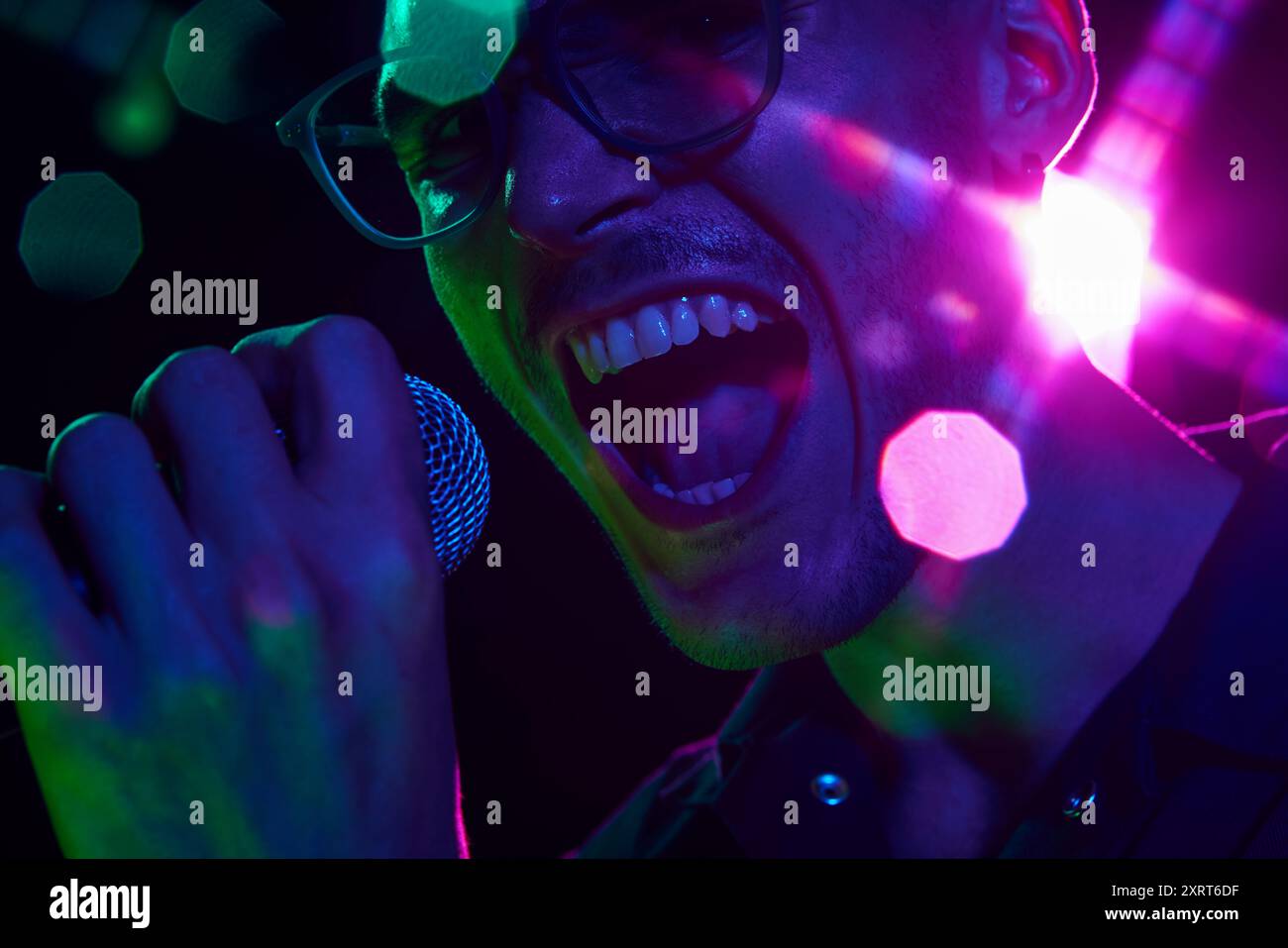 Vibrant neon hues highlight the intensity of vocalist in heat of performance, his powerful voice visible in every detail. Stock Photo