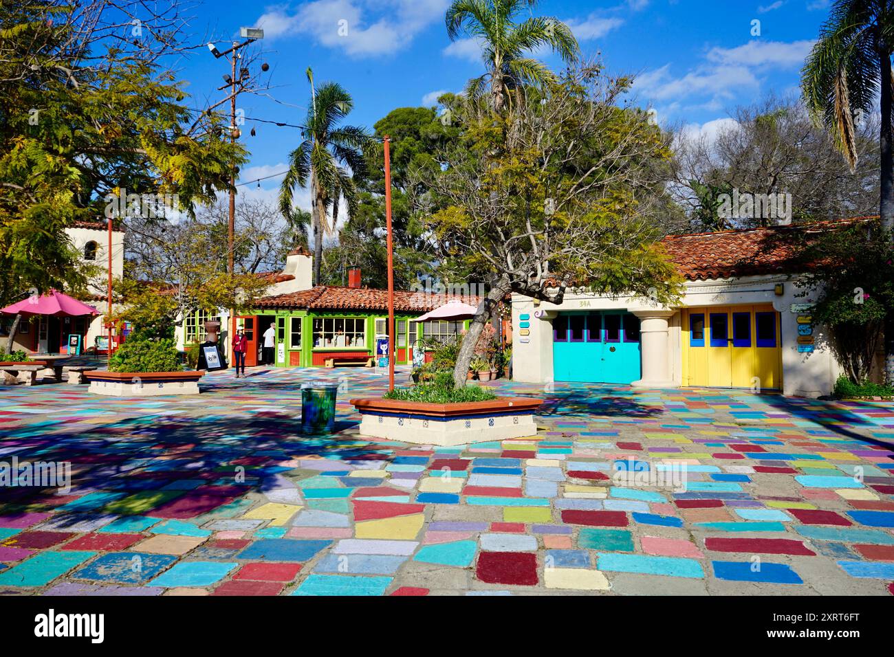 A vibrant, colorful plaza featuring multicolored tiles, lively buildings, and tropical greenery under a bright blue sky. Stock Photo