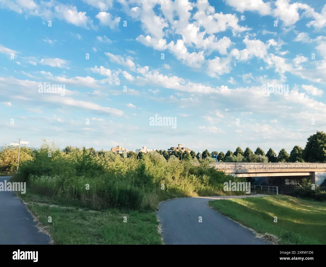 A bridge spans a river with a green field on either side. The sky is ...