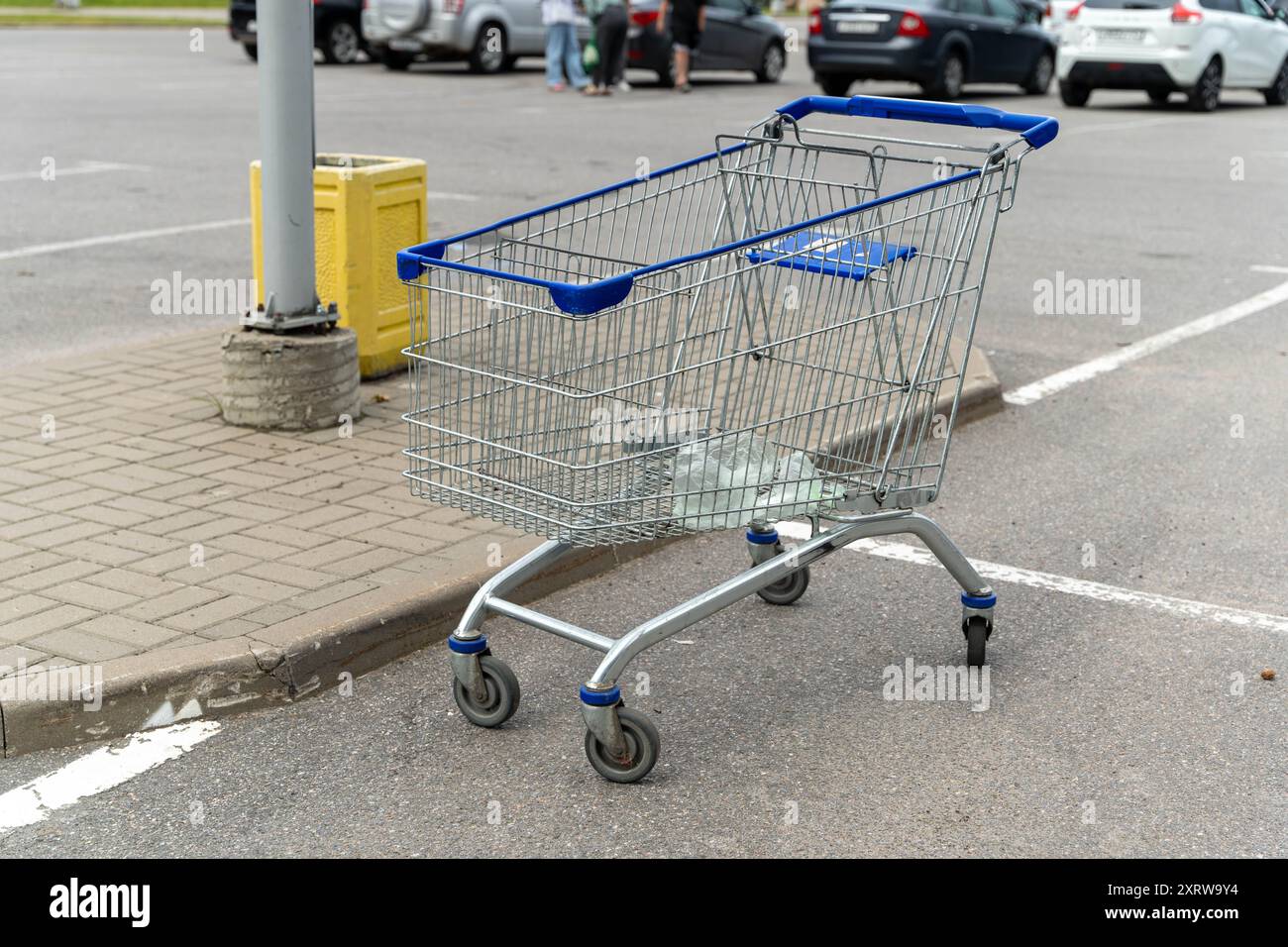 A shopping cart sits on the pavement, near a light pole, in a parking lot. Stock Photo