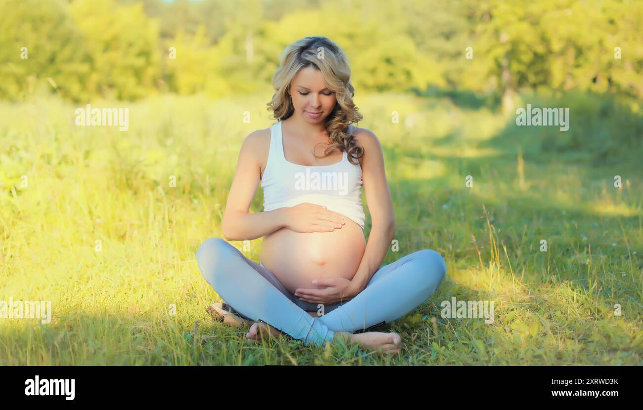 Happy young pregnant woman resting sitting on the grass in summer park ...